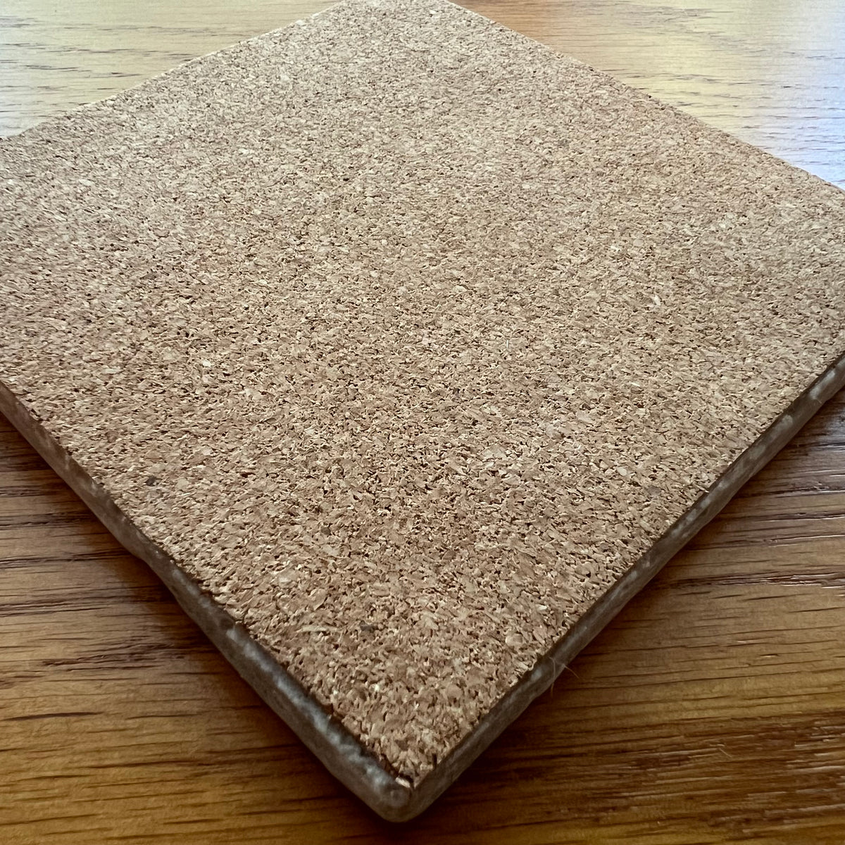 The reverse side of a square travertine coaster by Eclectic Spruce, showing that the bottom of the coaster is covered with a sturdy layer of cork to protect your tabletop from scratches.