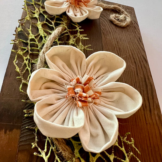 Close-up of the 3D botanical wall art featuring cream-colored flowers made from reclaimed fabric and mounted on a dark wood plank.
