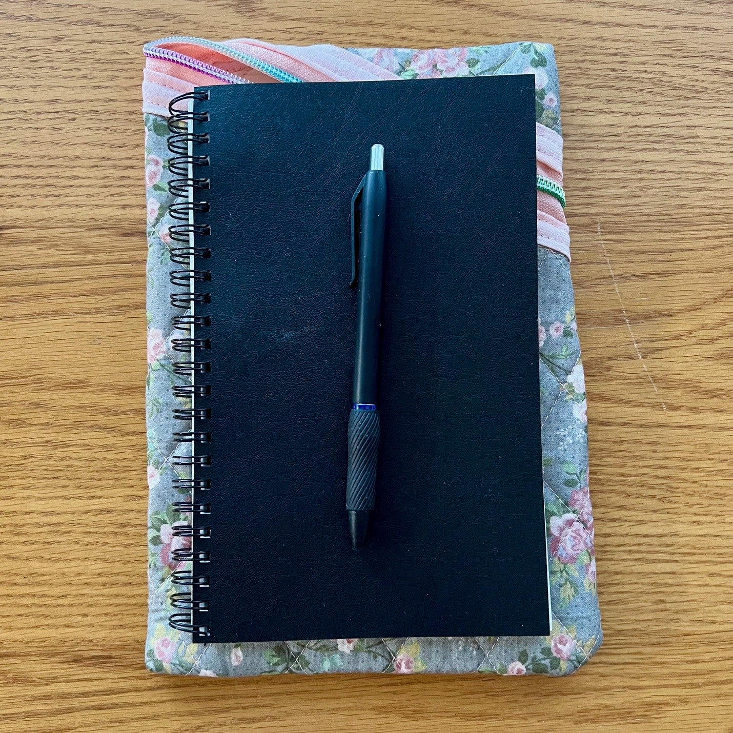 Floral zipper pouch with a journal and pen sitting on top to show sizing.