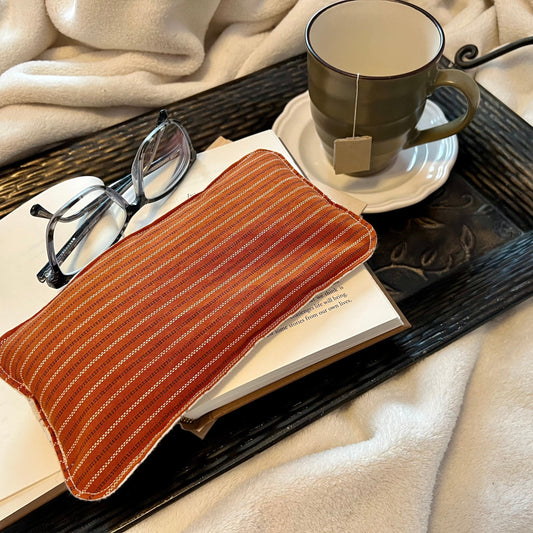 Weighted rest pillow sitting on a book next to a cup of tea and a cozy blanket