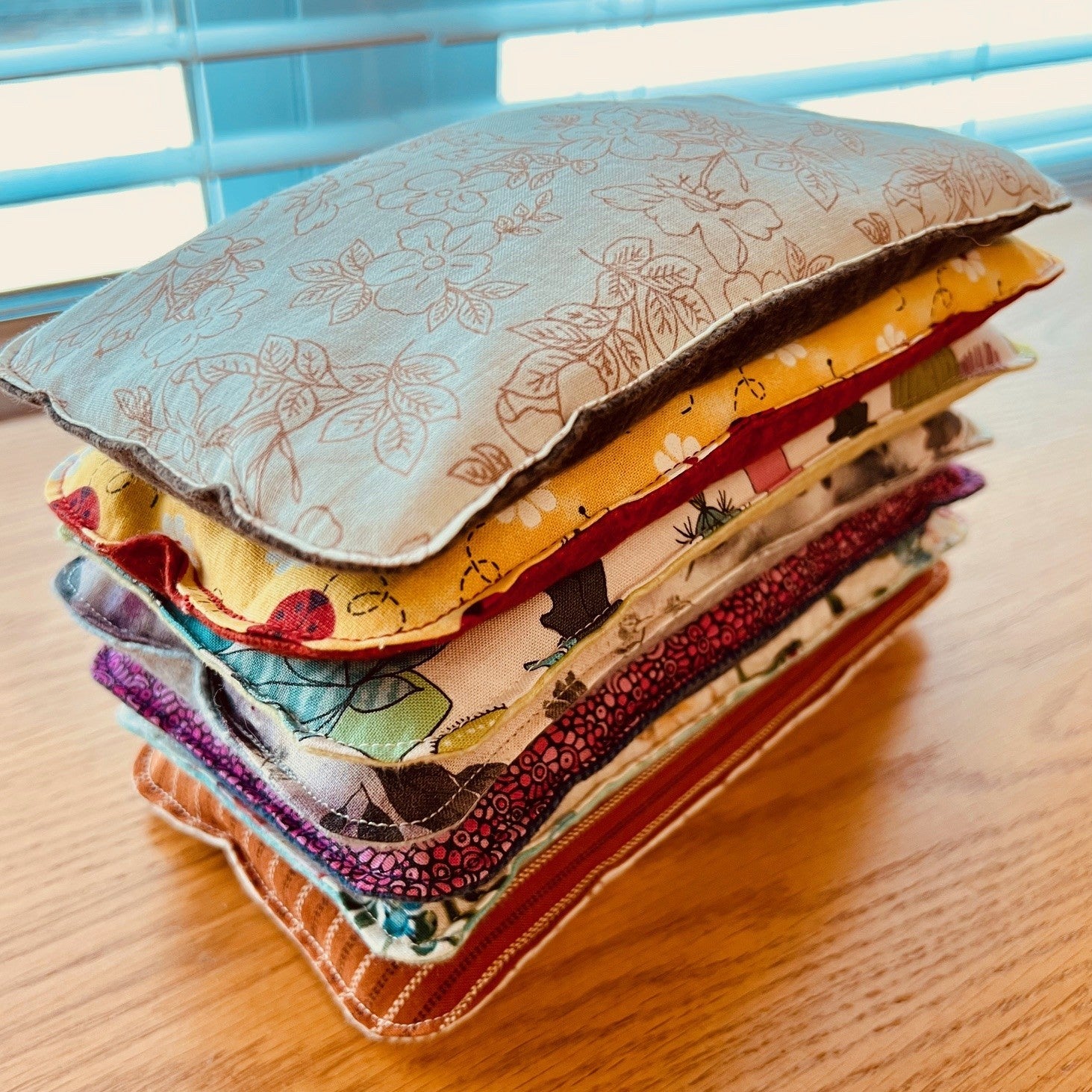 A stack of Eclectic Spruce Weighted Eye Pillows in with various colors and designs.