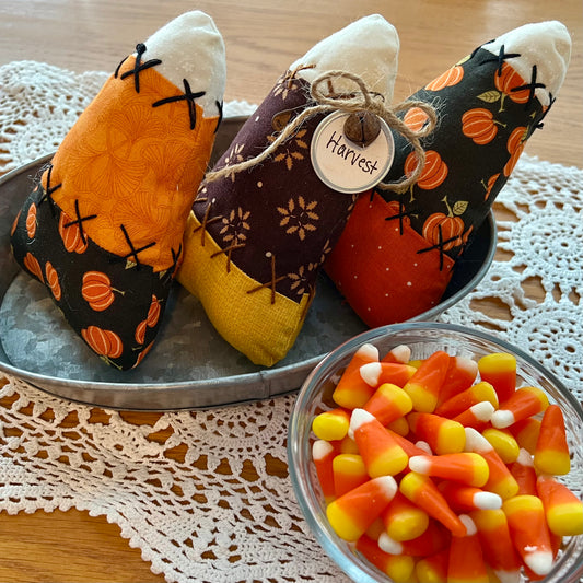 Three Eclectic Spruce handmade fabric candy corn bowl fillers with autumn harvest themes are arranged on a galvanized metal tray. The tray is sitting on a doily next to a glass bowl filled with candy corns.