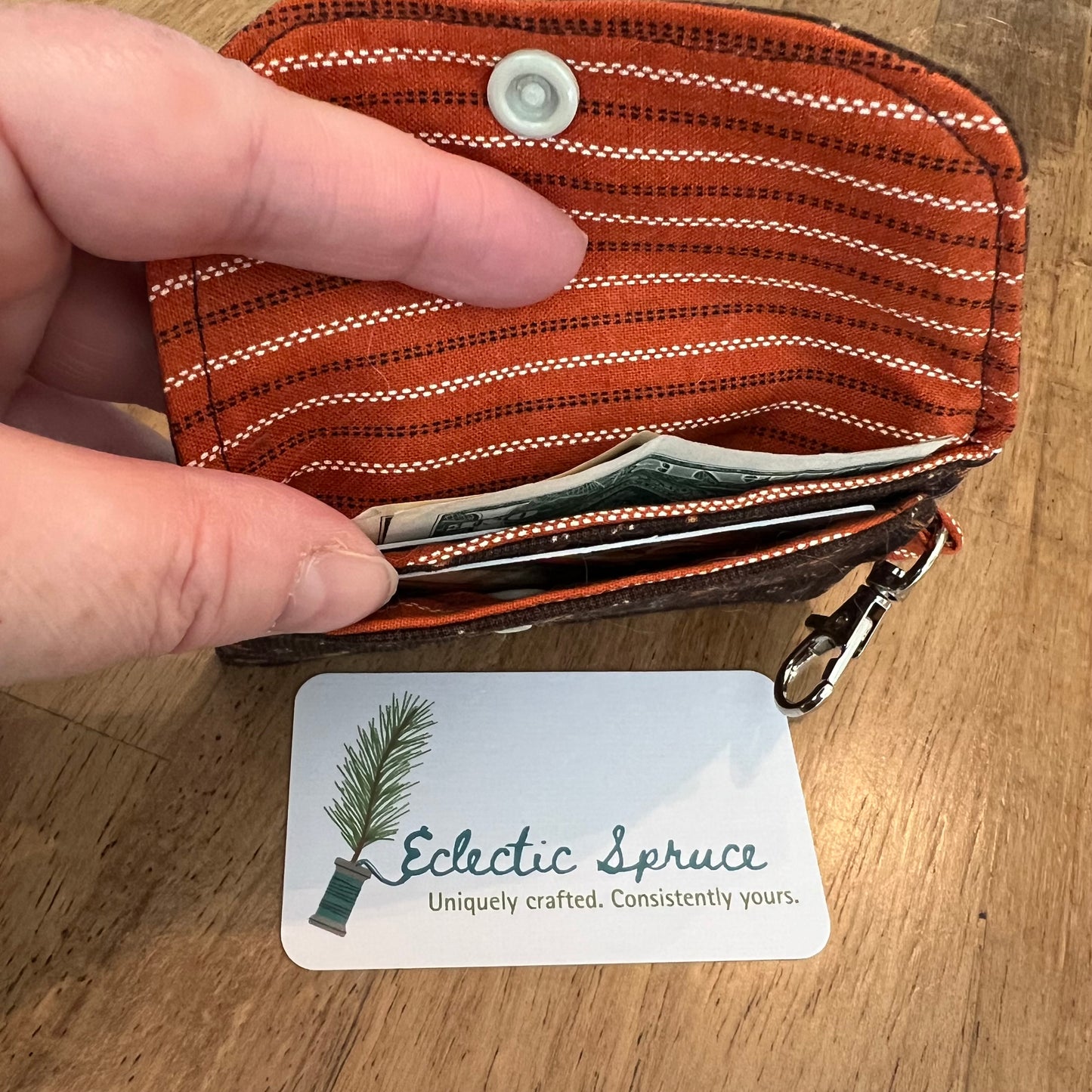Eclectic Spruce handcrafted mini card holder wallet shown open with cash and cards inside two card slots. The wallet has a dark brown floral exterior and rust striped interior and contains a beige snap closure and a silver metal swivel clasp for convenience and security.