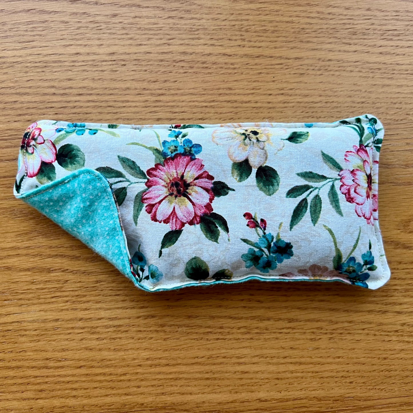 Dual-sided Weighted Eye Pillow with cream fabric containing pink, blue, and taupe flowers on the cotton side and aqua and with white polka dots on the flannel side.