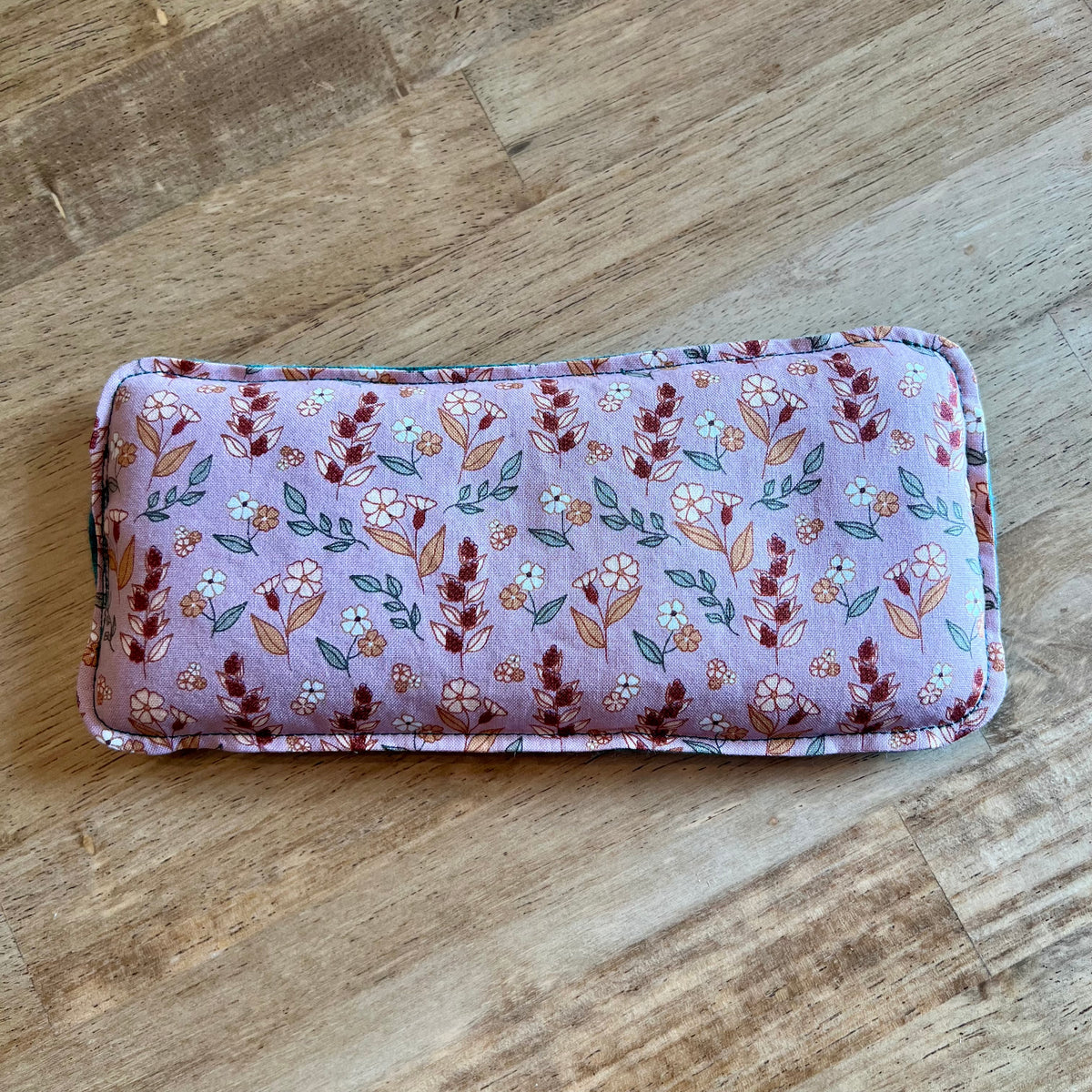 Dual-sided Evening Primrose Weighted Eye Pillow by Eclectic Spruce. This pillow features a mauve fabric with a floral pattern in red, green, white, and gold.