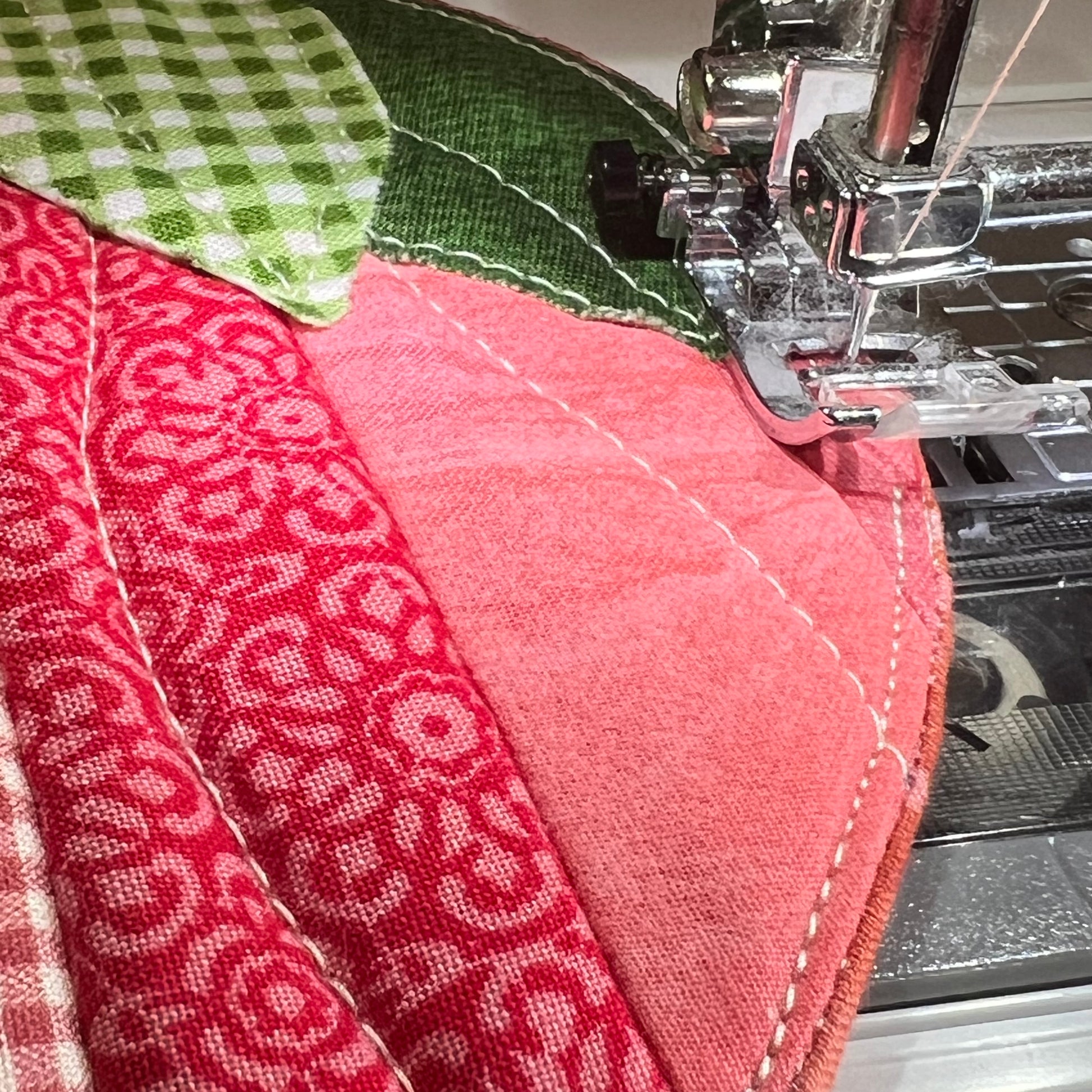 A closeup of a sewing machine topstitching an Eclectic Spruce Sweet Strawberry Hot Pad.