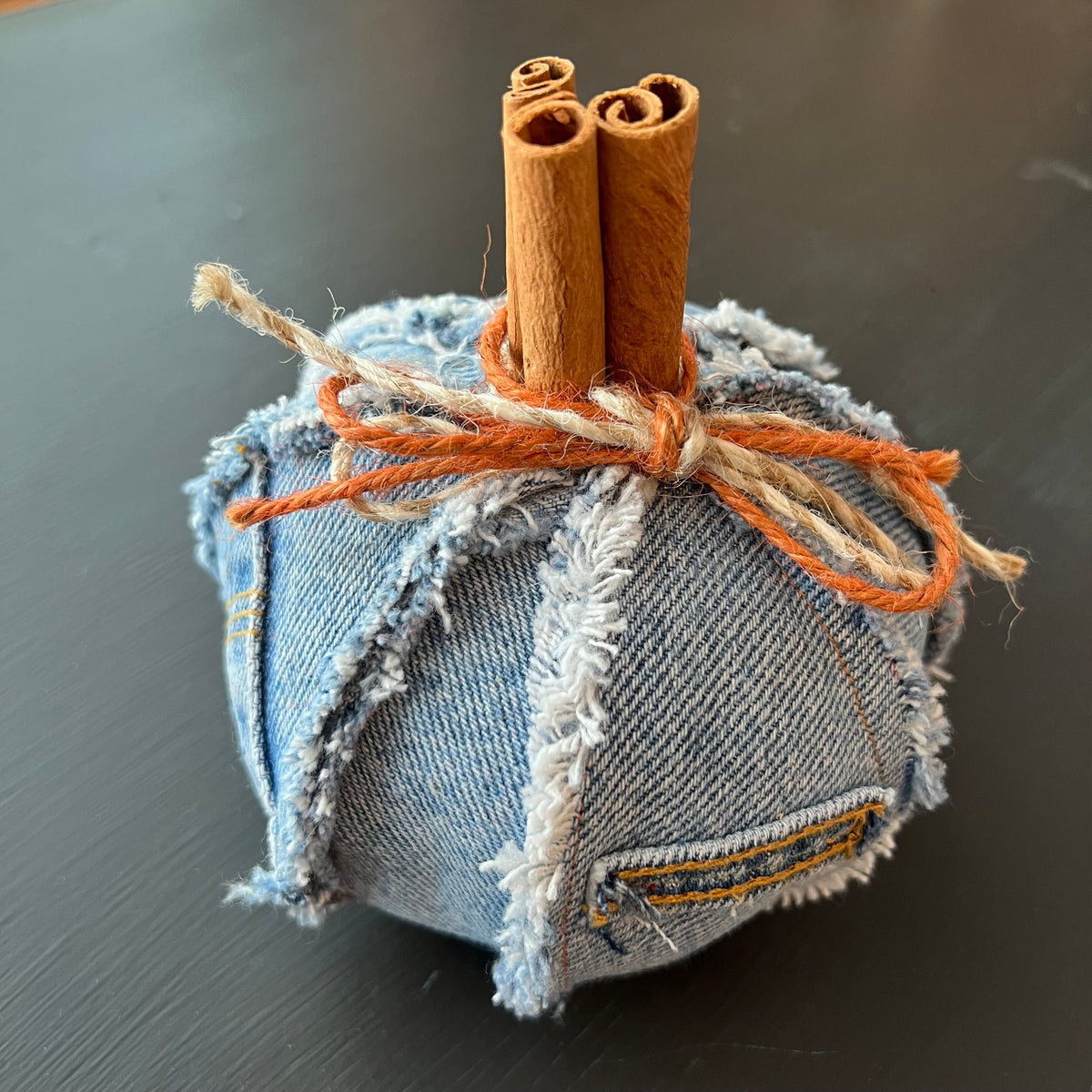Pumpkin 3: Handmade Eclectic Spruce small pumpkin made with frayed denim fabric and real cinnamon stick stems, accented with prominent frayed seam accents and a twine bow.