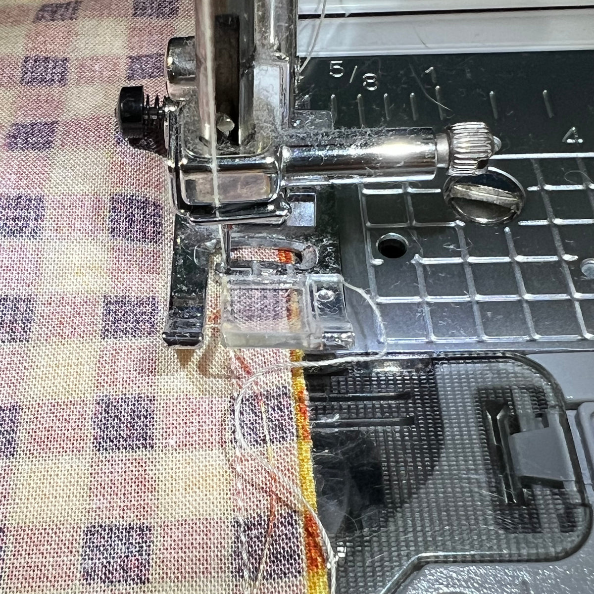 Close-up of a sewing machine needle and presser foot stitching a checkered fabric. This is an example photo from the Eclectic "Purrfect Patchwork Cat Pillows" sewing pattern.