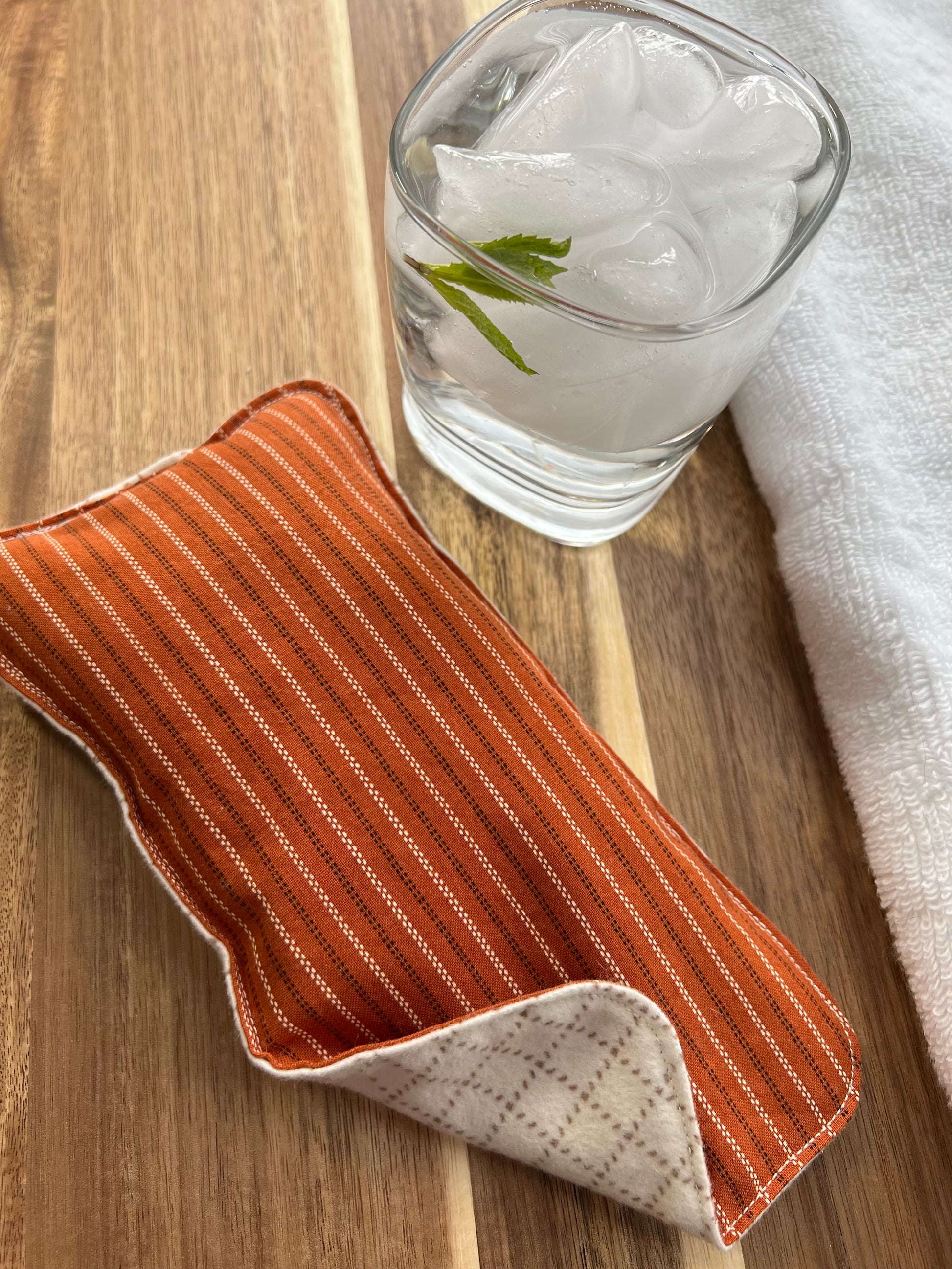Weighted eye pillow on a wood surface next to a white towel and glass of ice water.