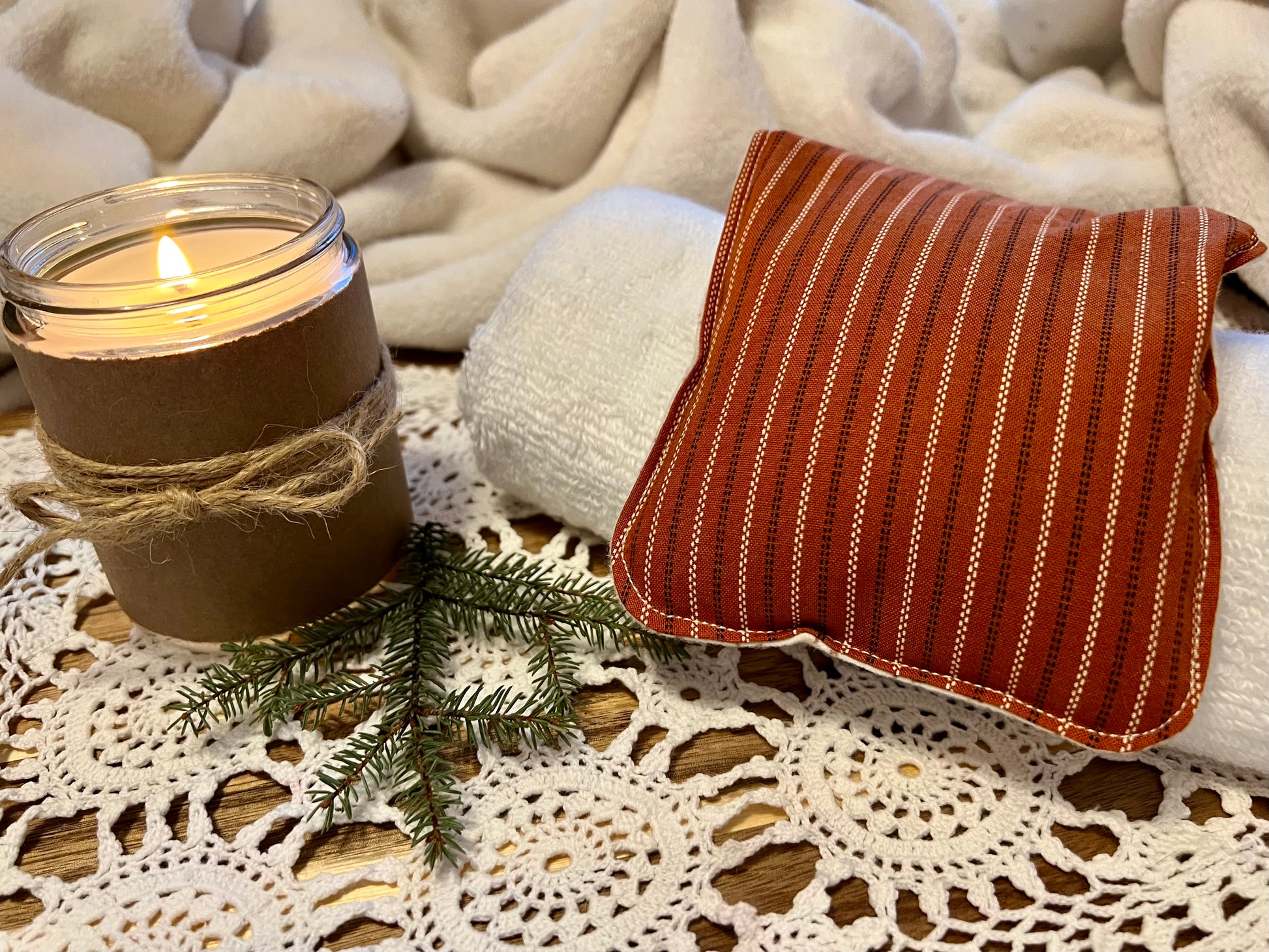 Weighted Eye Pillow on a lace tablecloth next to a lit candle and a warm cozy blanket.