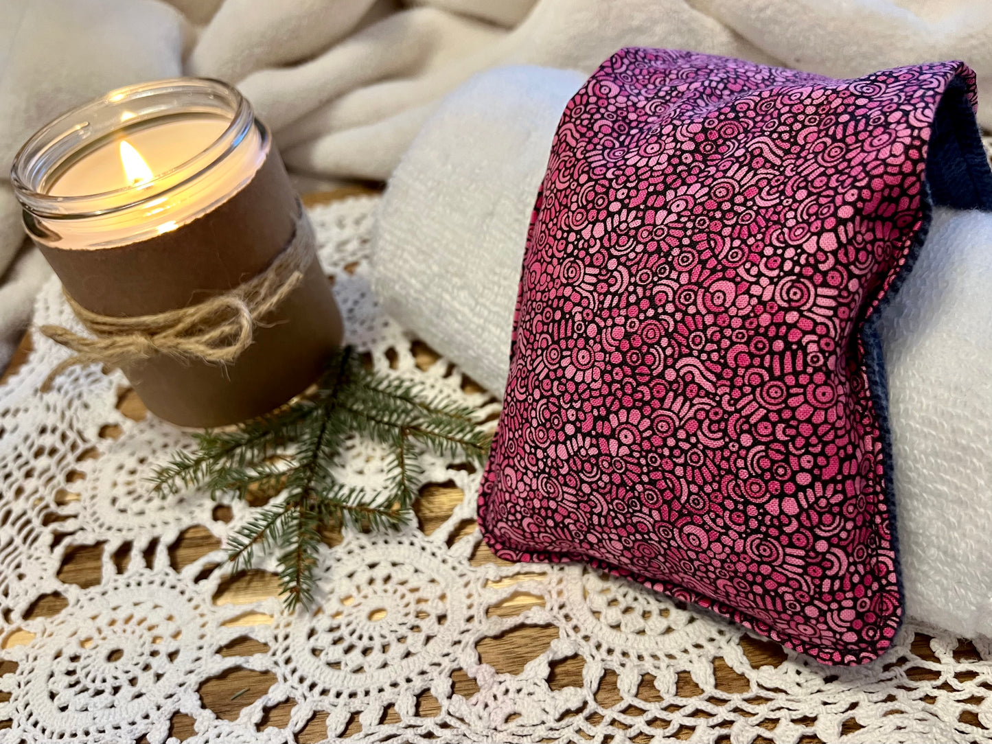 Weighted Eye Pillow on a lace tablecloth next to a lit candle and a warm cozy blanket.