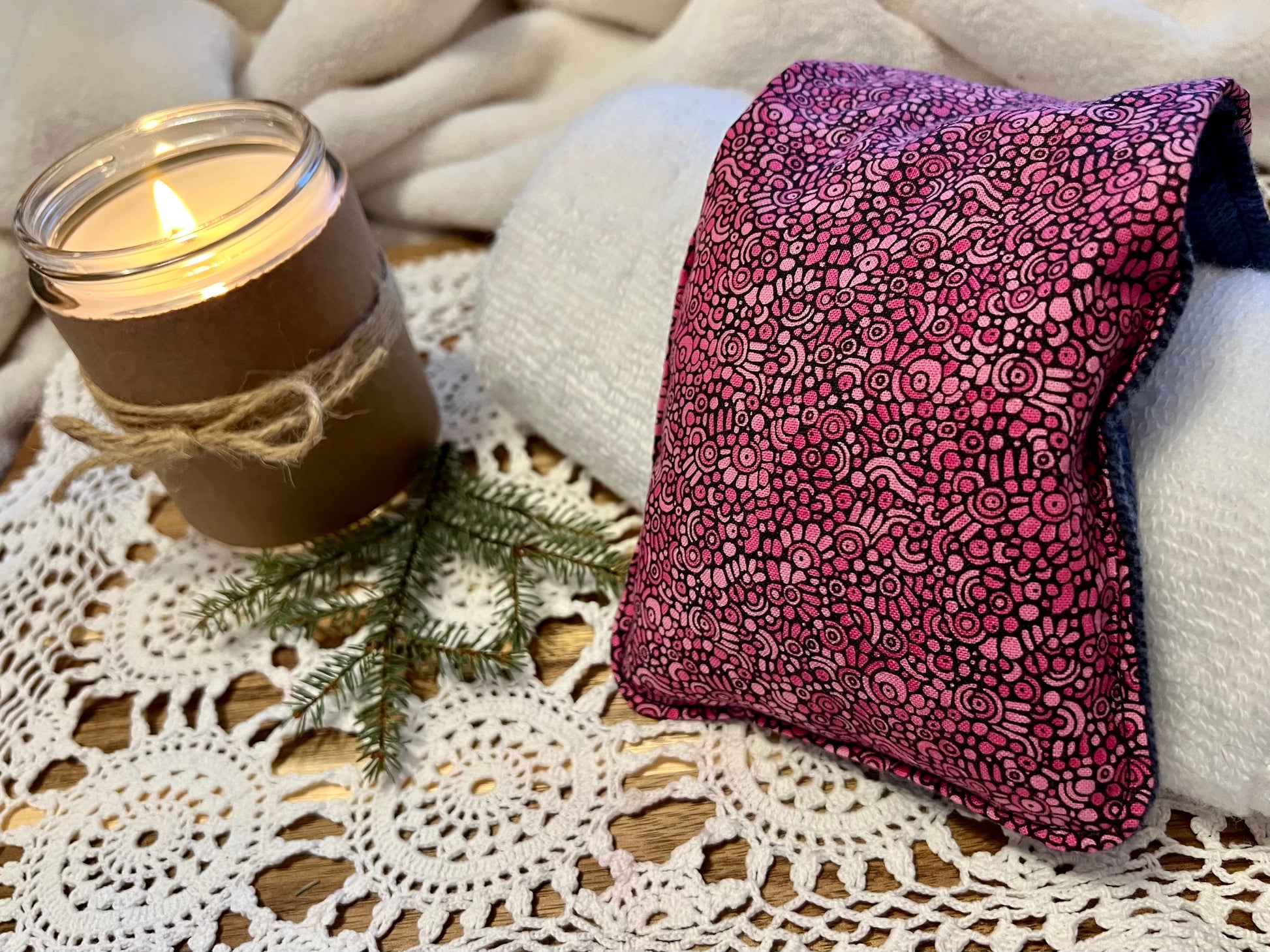 Weighted Eye Pillow on a lace tablecloth next to a lit candle and a warm cozy blanket.