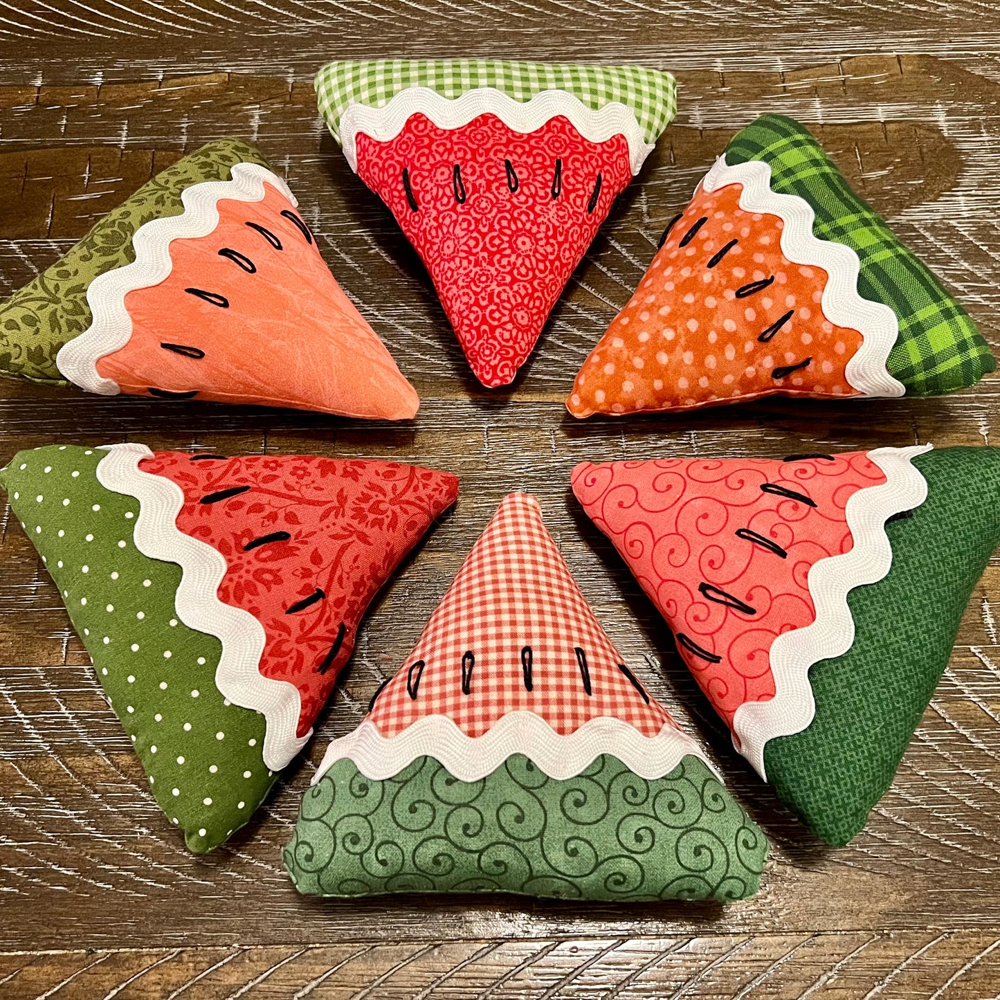 Six fabric watermelon slices on a wooden surface - this photo shows all the designs that are possible for you to receive with your trio.