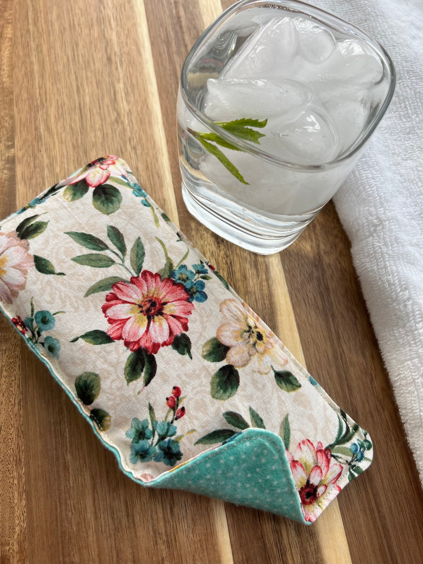 Weighted Eye Pillow on a wood surface next to a white towel and glass of ice water.