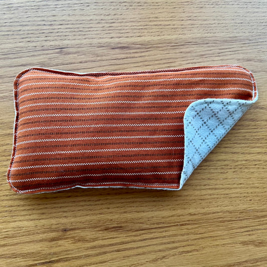 Dual-sided Weighted Eye Pillow with rust fabric lined with brown and cream stripes on the cotton side and a cream and brown diamond pattern on the flannel side.