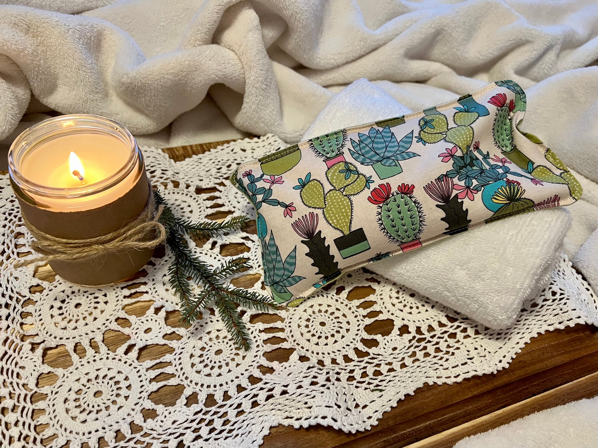 Weighted Eye Pillow on a lace tablecloth next to a lit candle and a warm cozy blanket.