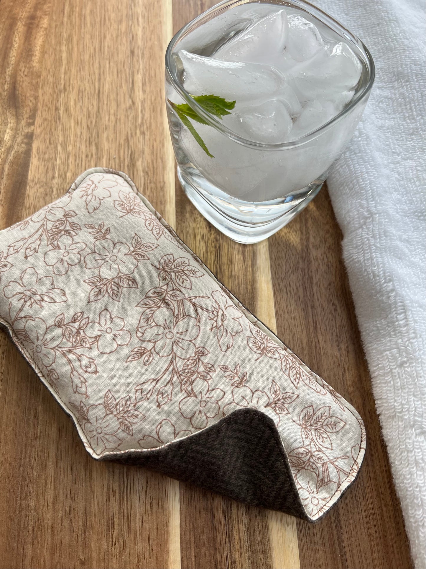 Weighted Eye pillow on a wood surface next to a white towel and glass of ice water.
