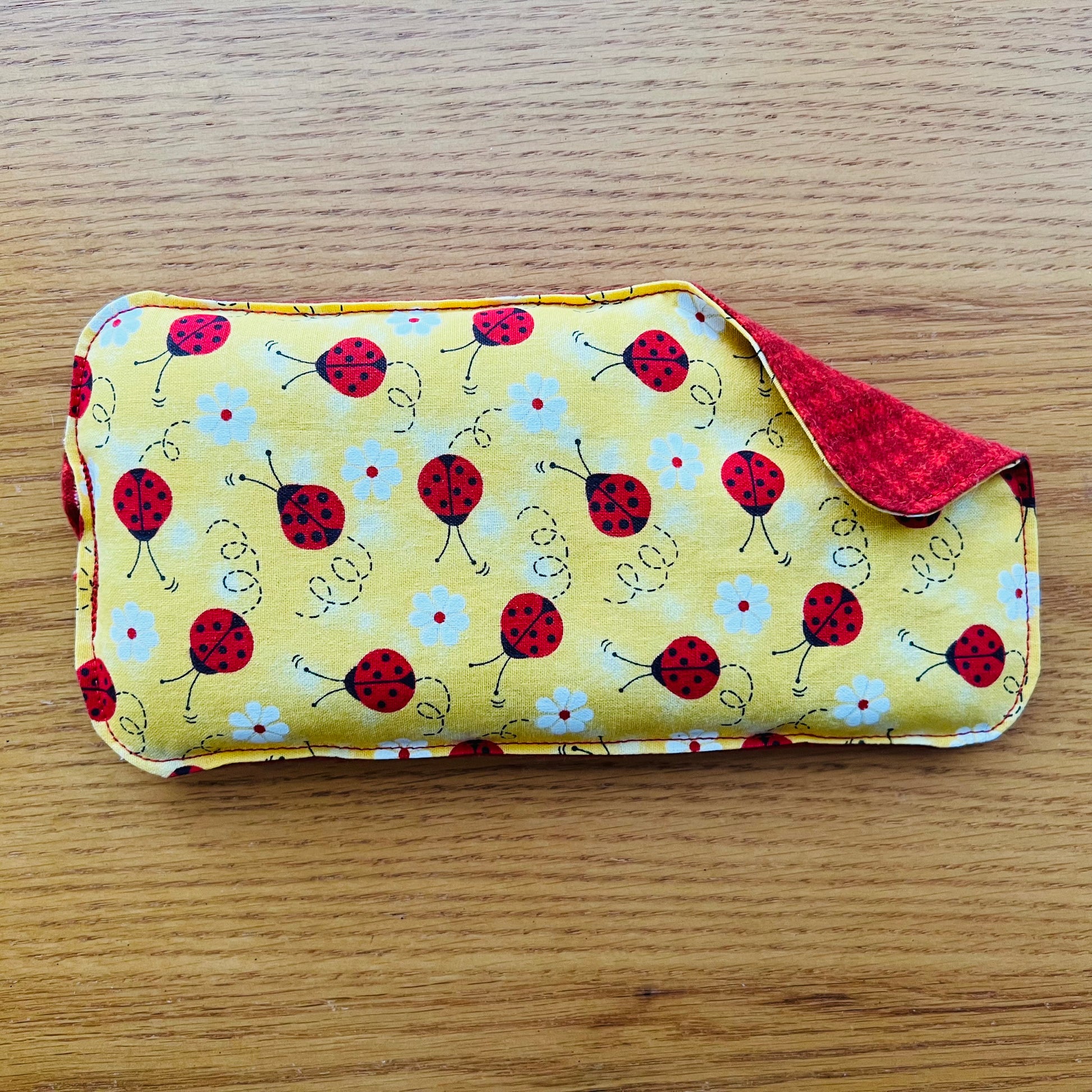 Dual-sided Weighted Eye Pillow with yellow fabric patterned with red ladybugs and white daisies on the cotton side and red houndstooth pattern on the flannel side.