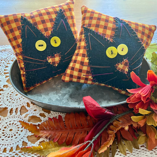 Example of two handmade Eclectic Spruce Purrfect Patchwork Cat Pillows. These are 5x5 inch decorative square pillows with black cat faces and orange plaid background, displayed in a metal tray with autumn leaves and flowers on a lace doily.