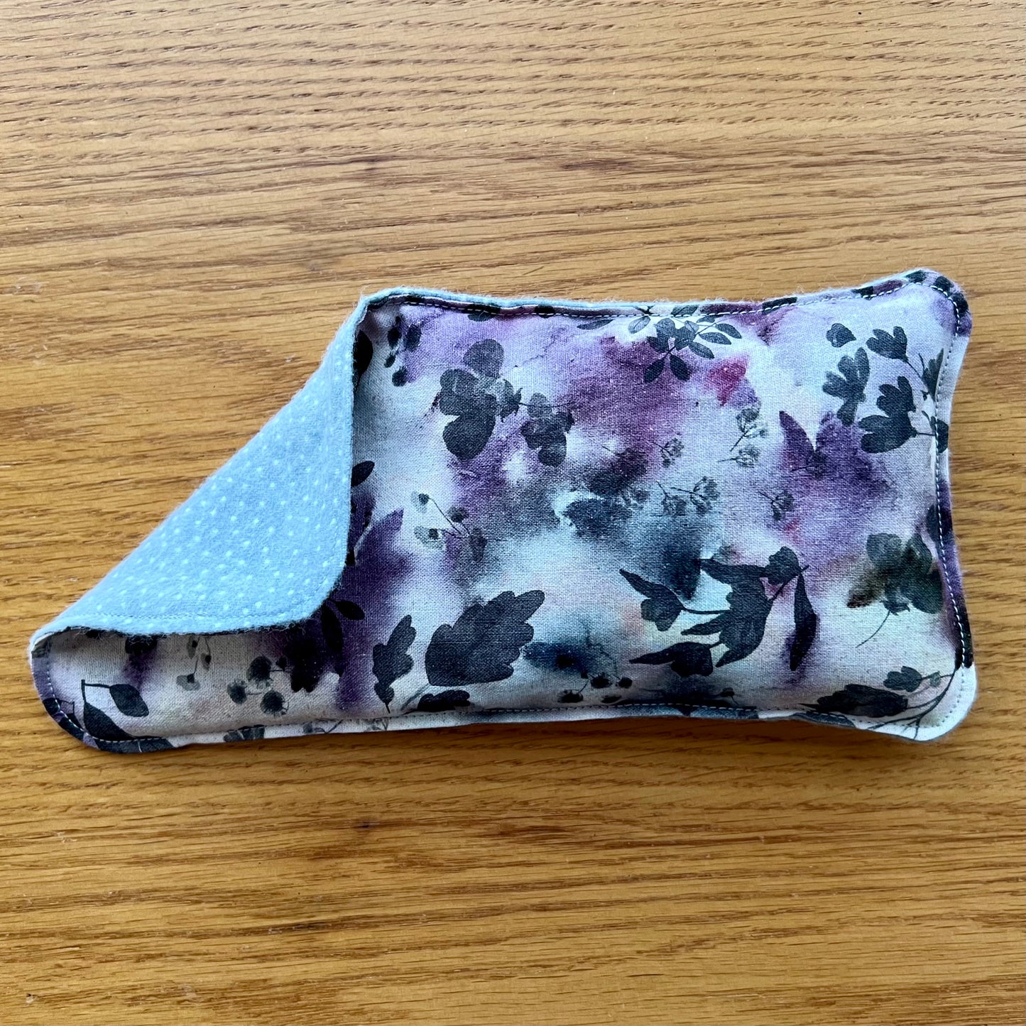 Dual-sided Weighted Eye Pillow with a purple floral pattern with dark leaves on the cotton side and light grey and white polka dots on the flannel side.