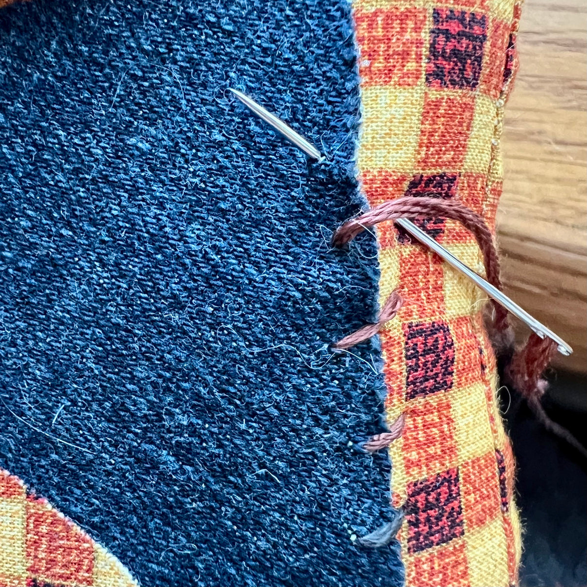 Close-up of a needle stitching the cat applique to a decorative pillow. This is an example photo from the Eclectic "Purrfect Patchwork Cat Pillows" sewing pattern.