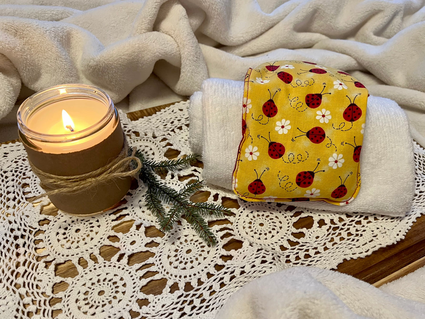 Weighted Eye Pillow on a lace tablecloth next to a lit candle and a warm cozy blanket.