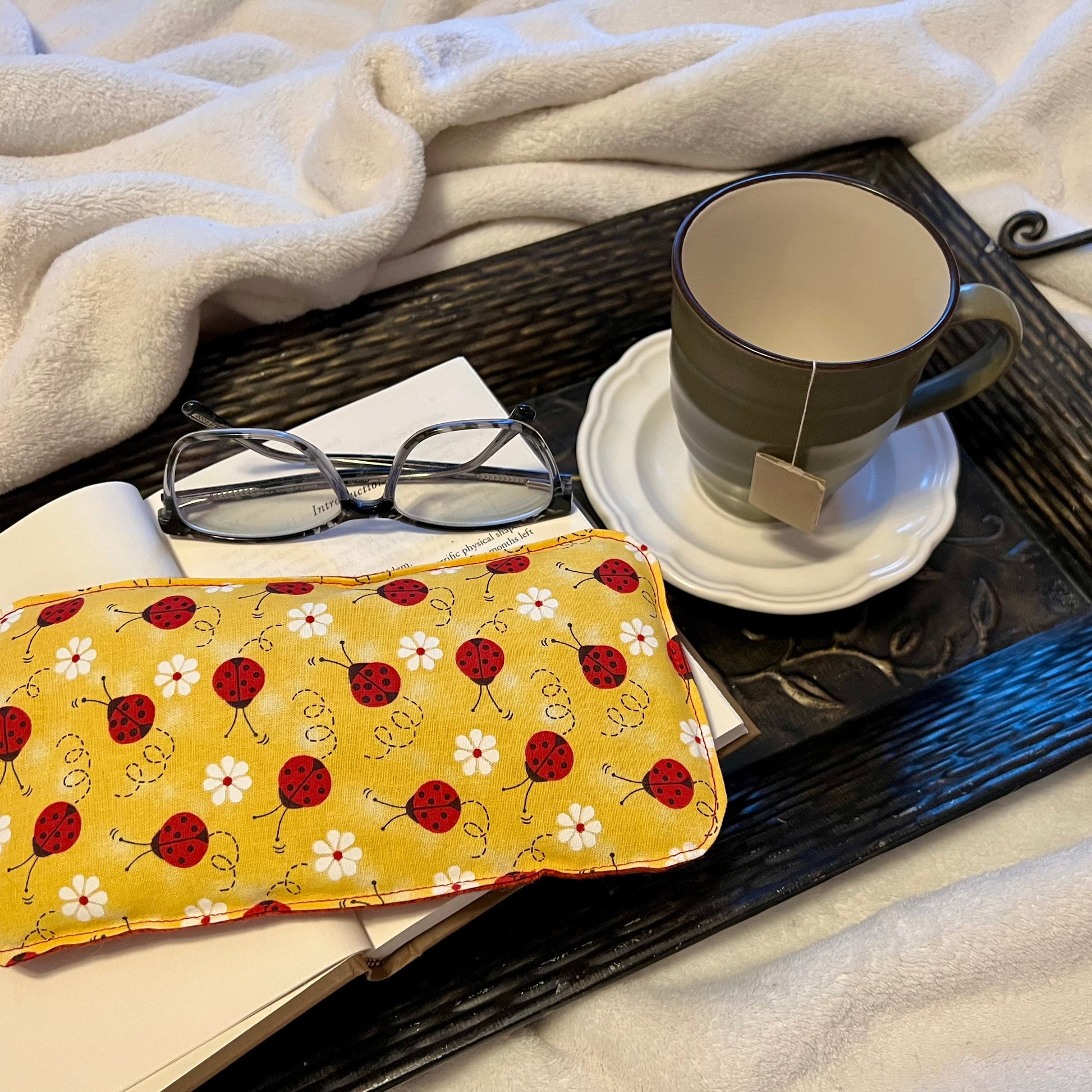 Tray with book, Weighted Eye Pillow, and mug on a soft blanket.