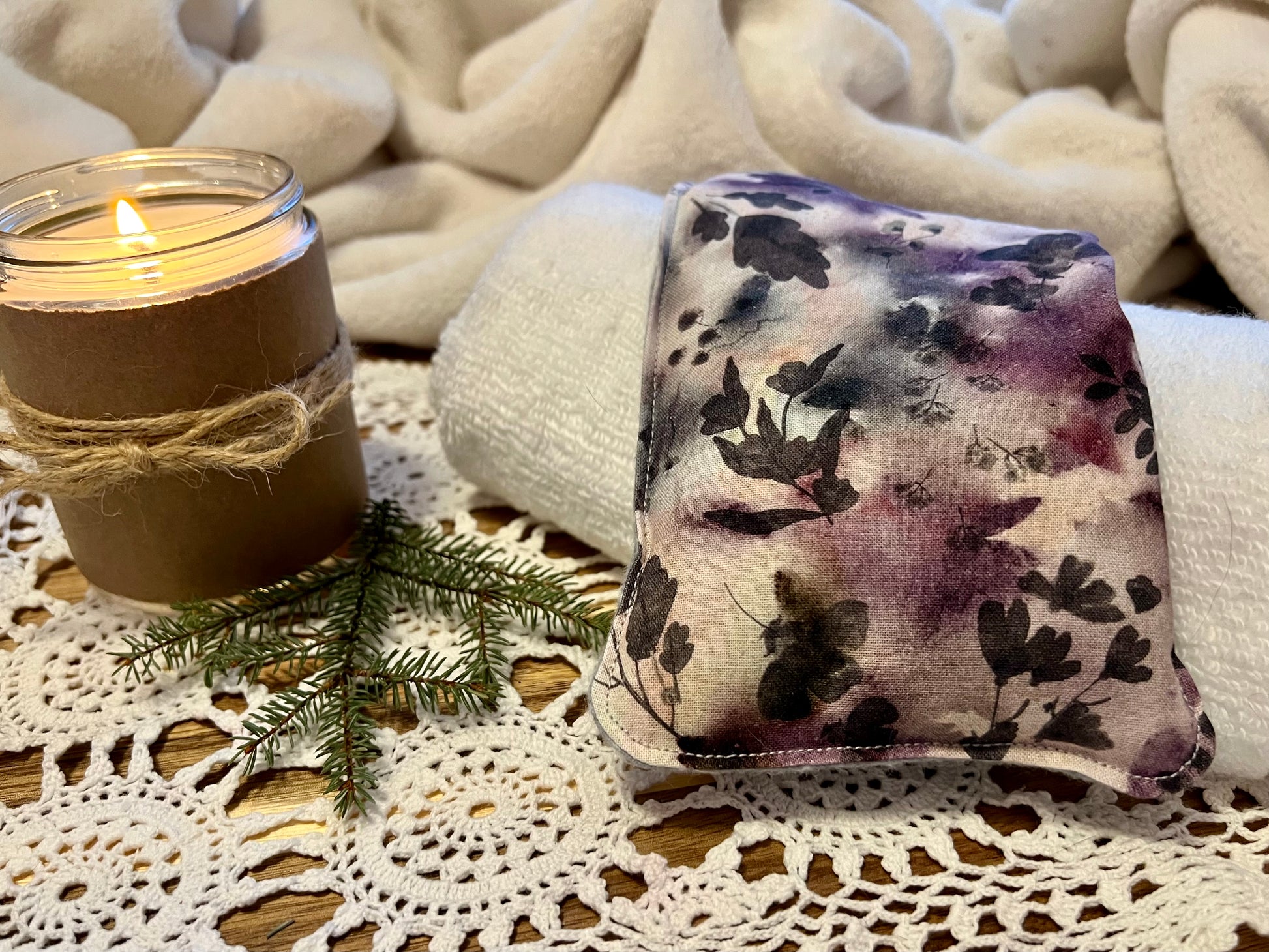 Weighted Eye Pillow on a lace tablecloth next to a lit candle and a warm cozy blanket.