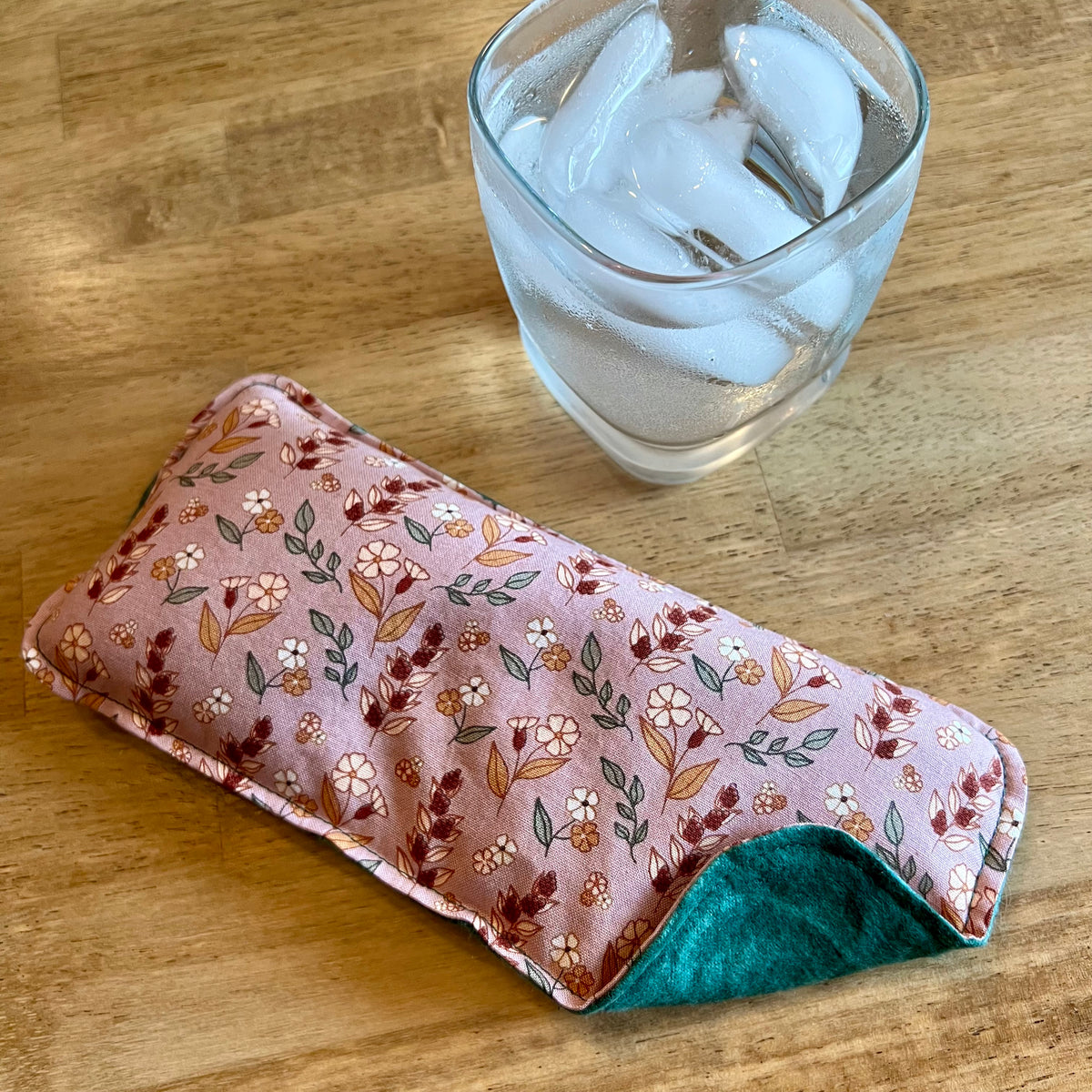 An Eclectic Spruce Evening Primrose Weighted Eye pillow on a wood surface next to a glass of ice water.