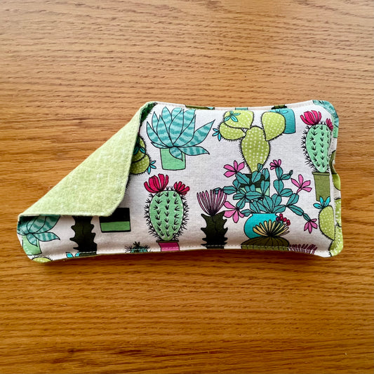 Dual-sided Weighted Eye Pillow with cream fabric patterned with colorful cacti on the cotton side and light green on the flannel side.