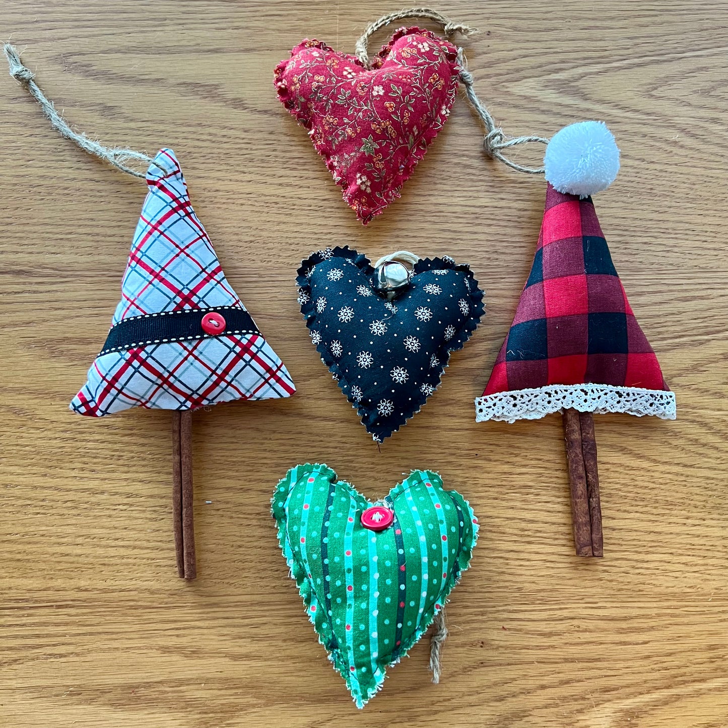 This photo shows a mystery style curated combination of Eclectic Spruce heart and cinnamon tree ornaments. This photo (shown as an example) shows 3 hearts and 2 cinnamon trees sitting on a wood surface.