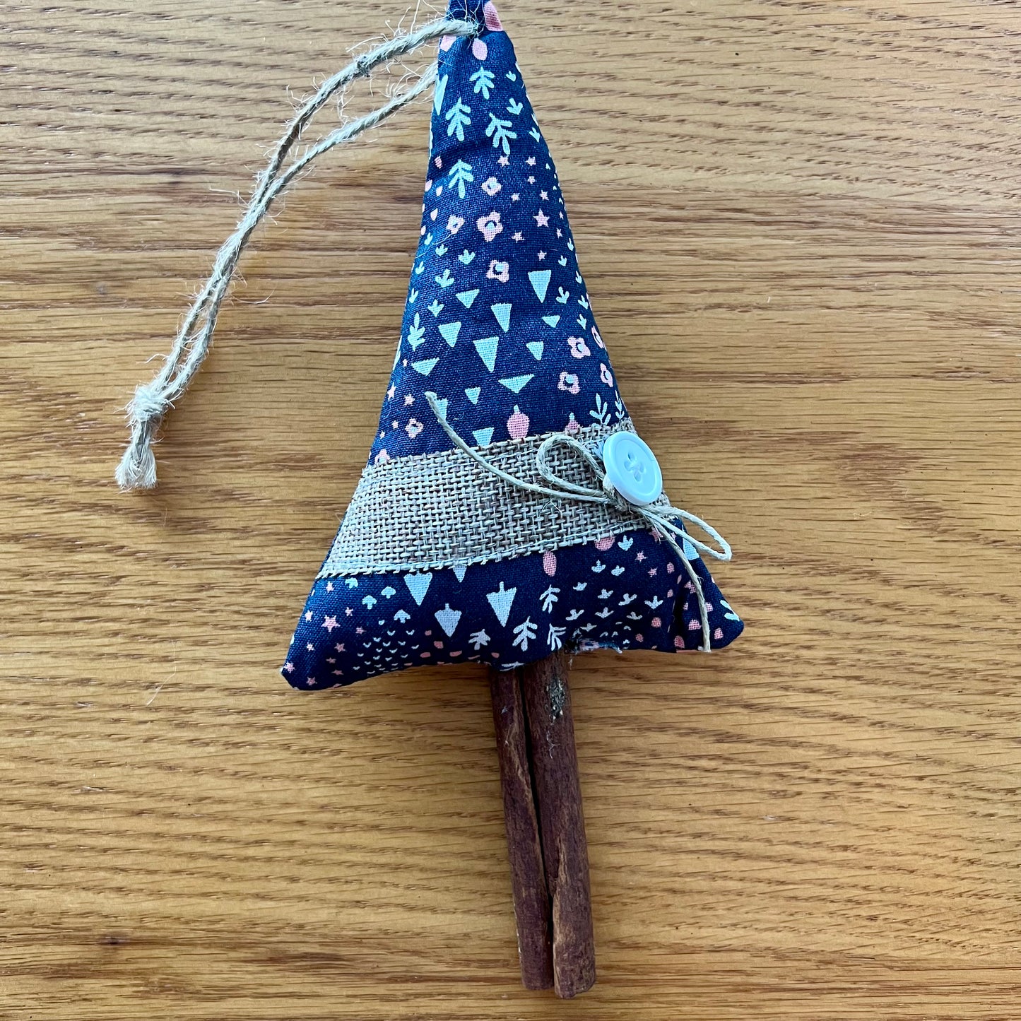 Eclectic Spruce's handmade cinnamon stick trees are made with cotton fabric, stuffed with fiberfill, and embellished with real cinnamon sticks along with lace, buttons, bells, and other trim.  Sold mystery style, you will receive a unique tree picked out just for  you. This photo shows ONE Eclectic Spruce tree sitting on a wood surface.
