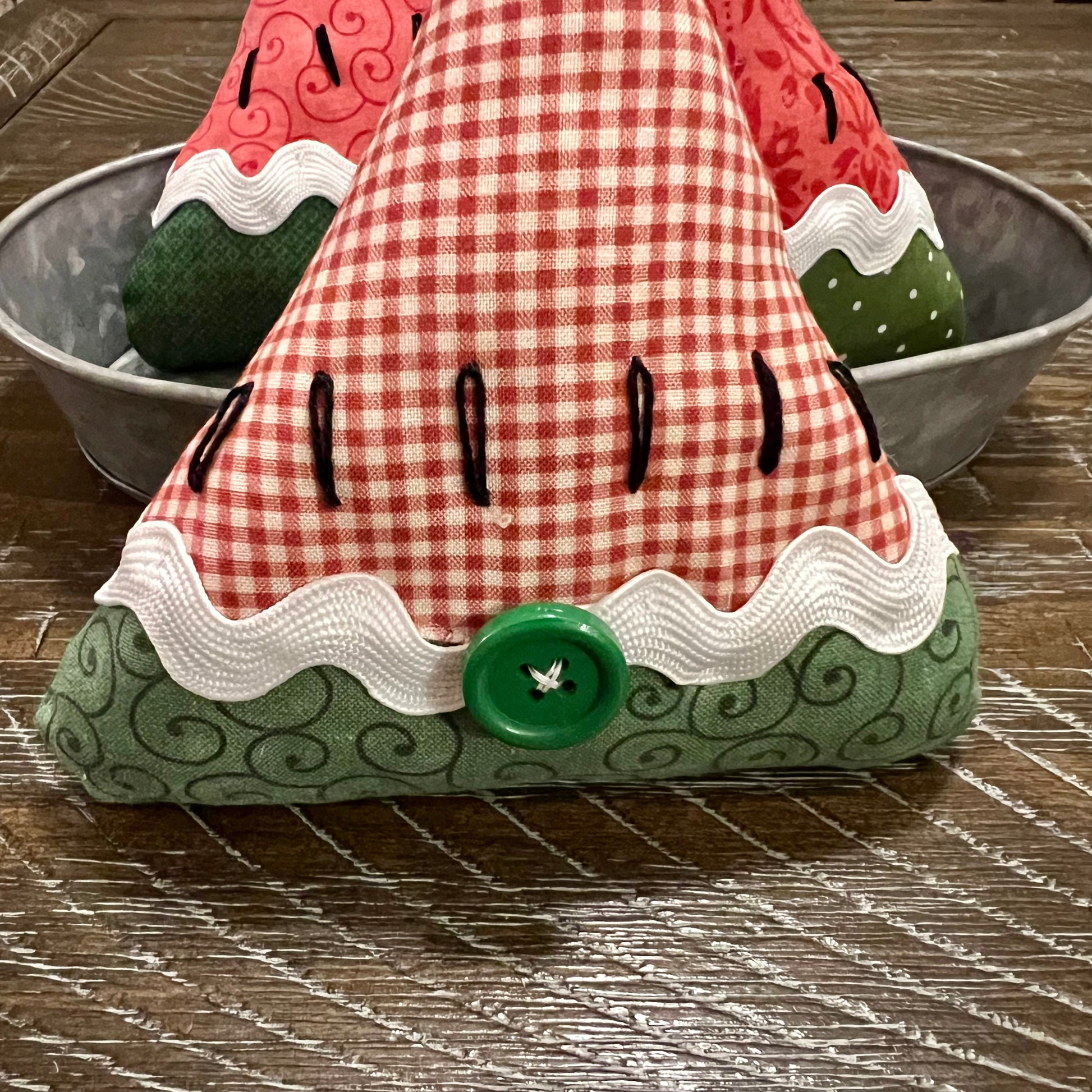 Decorative watermelon-shaped bowl filler with a checkered pattern on a wooden surface. This photo shows the button on the back that hides the seam in the rick rack trim.
