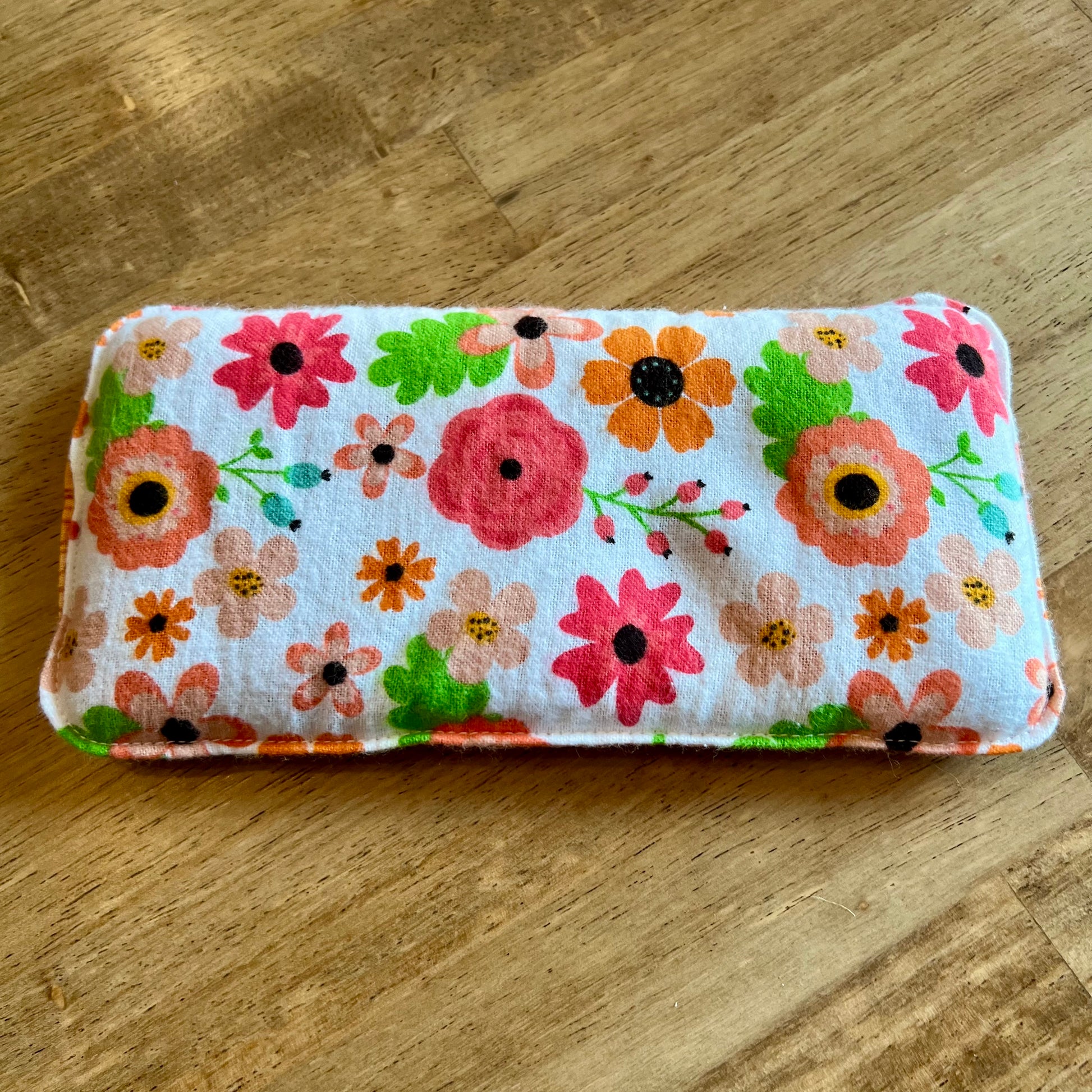 Dual-sided Retro Bloom Weighted Eye Pillow by Eclectic Spruce. This pillow features a colorful floral print with pink, orange, and green flowers on a white background.
