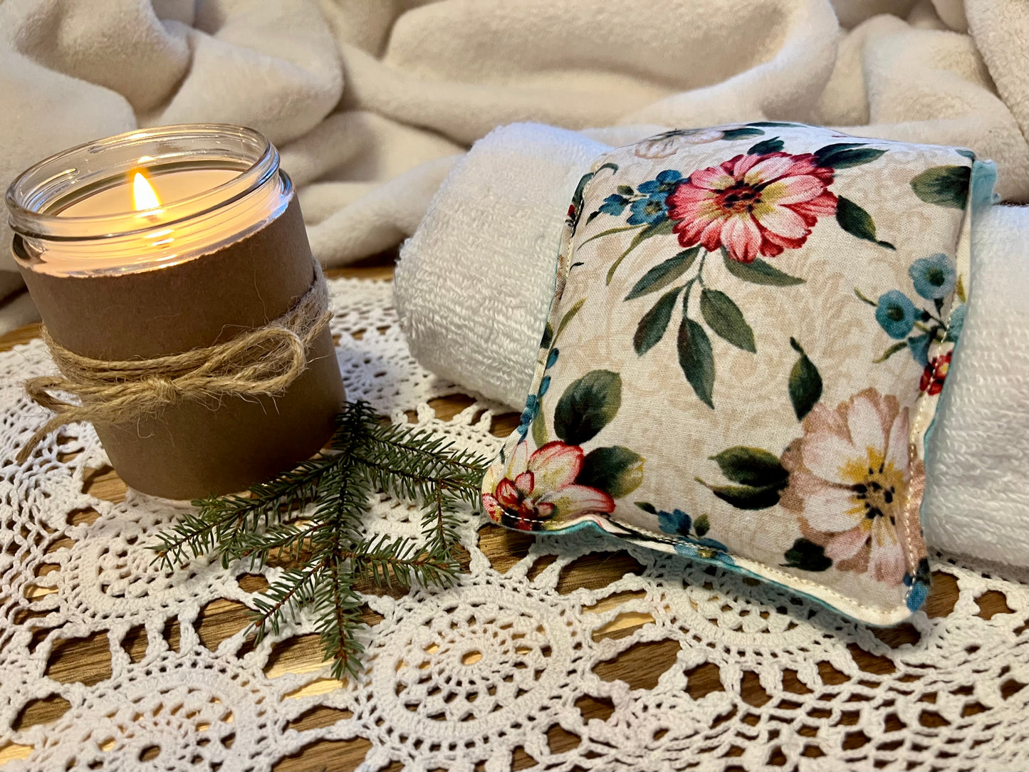 Weighted Eye Pillow on a lace tablecloth next to a lit candle and a warm cozy blanket.