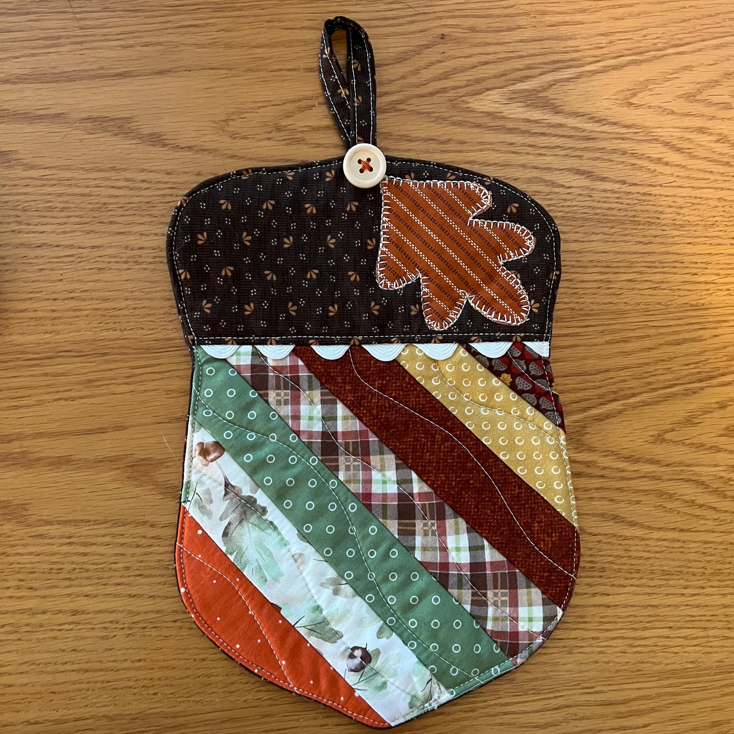 Option B: One Eclectic Spruce acorn-shaped quilted potholder with autumn-themed patchwork fabrics, applique leaf design, wood button, rick rack detailing, and hanging loop.