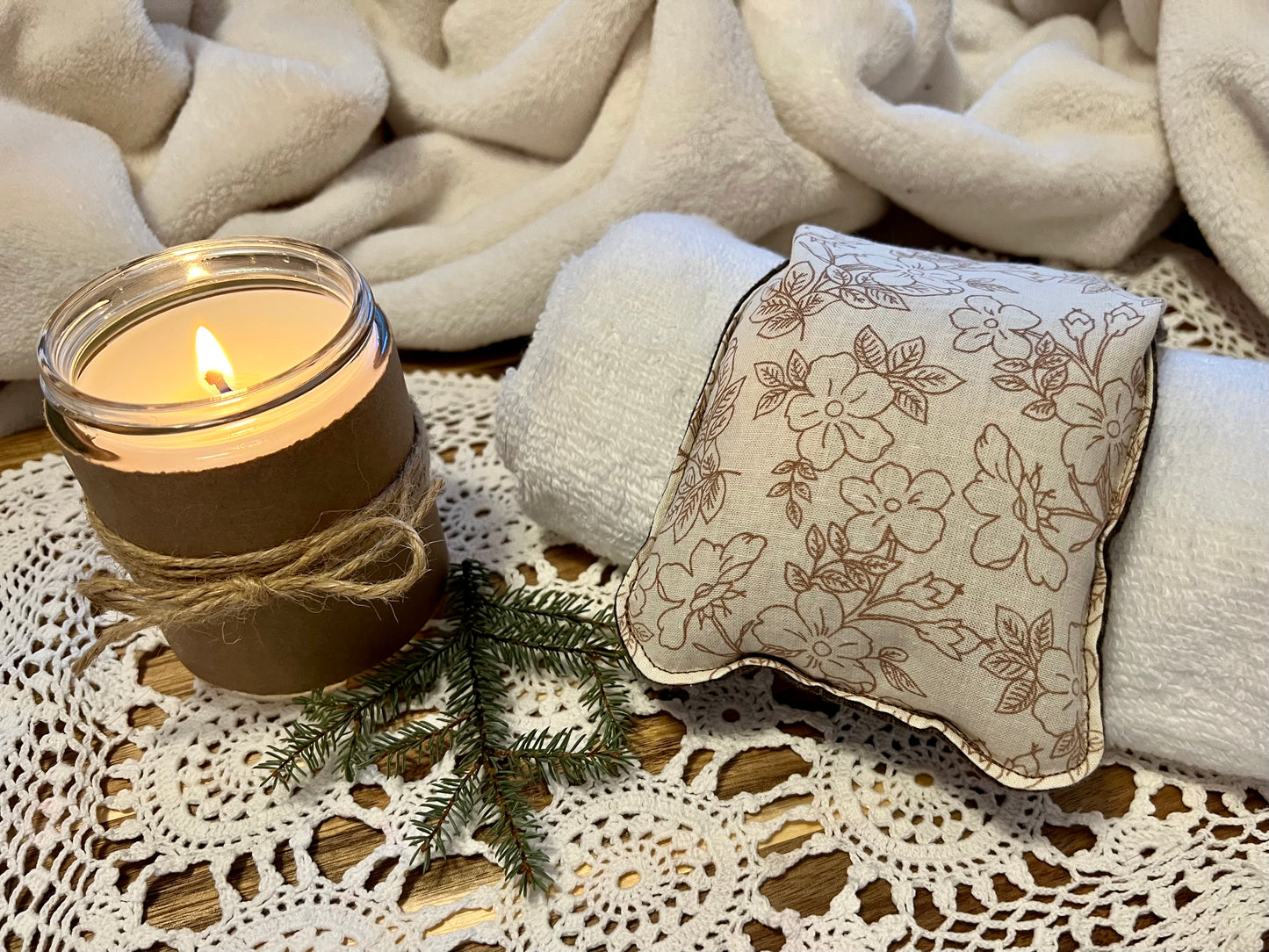 Weighted Eye Pillow on a lace tablecloth next to a lit candle and a warm cozy blanket.