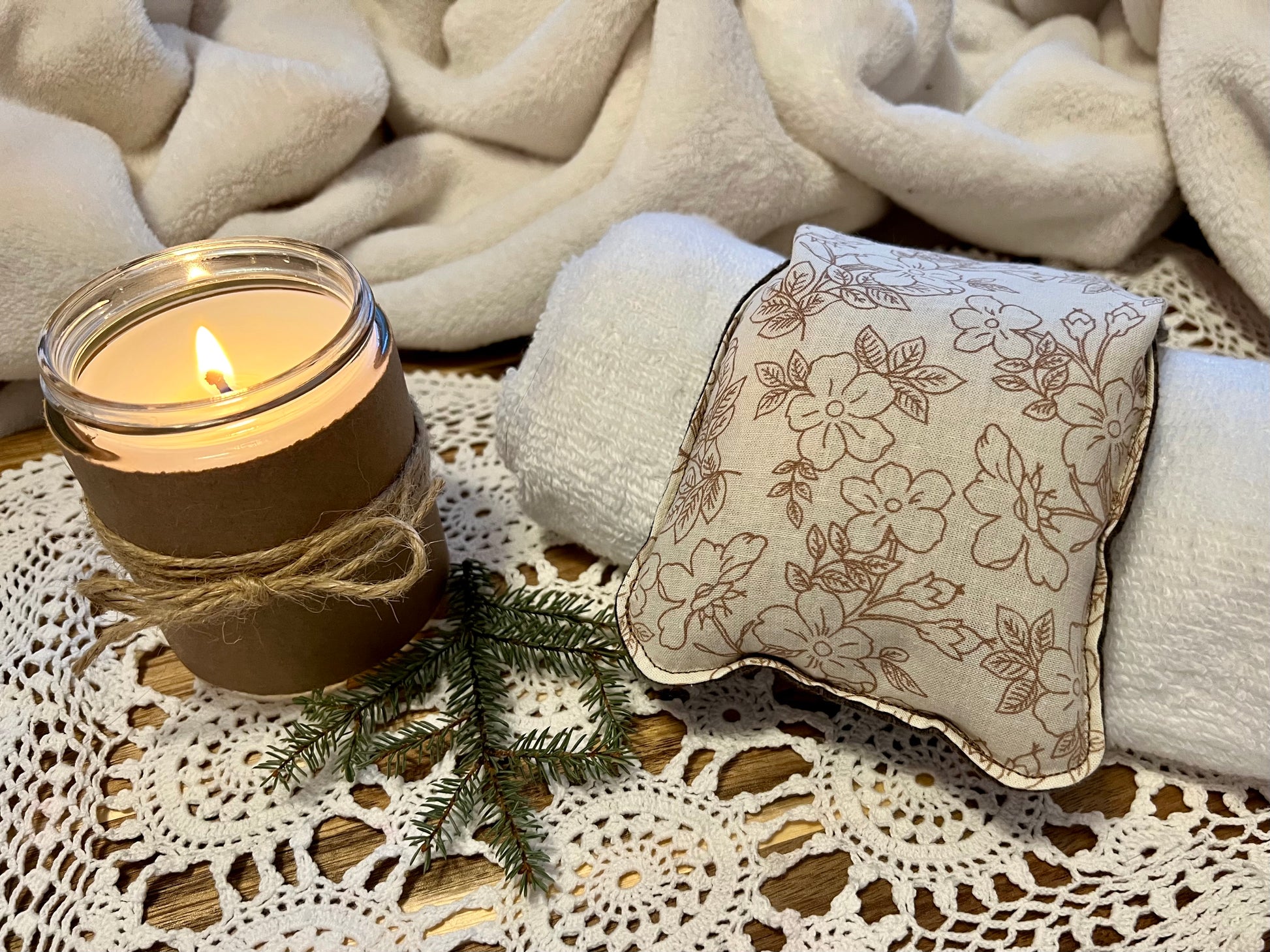 Weighted Eye Pillow on a lace tablecloth next to a lit candle and a warm cozy blanket.