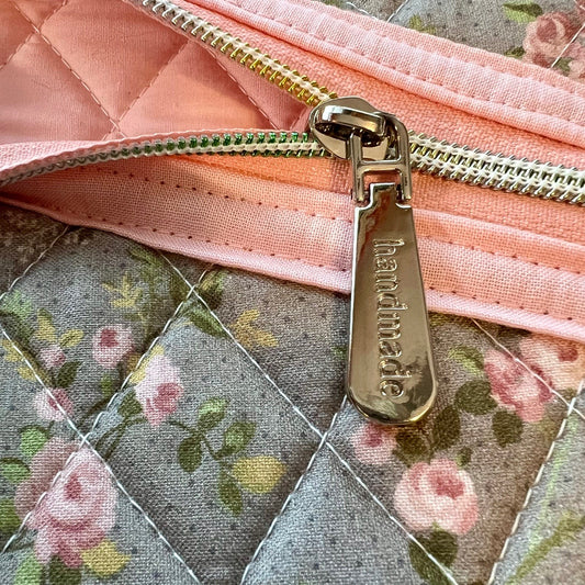 Close up of floral quilted zipper pouch, featuring a silver zipper that says "handmade."