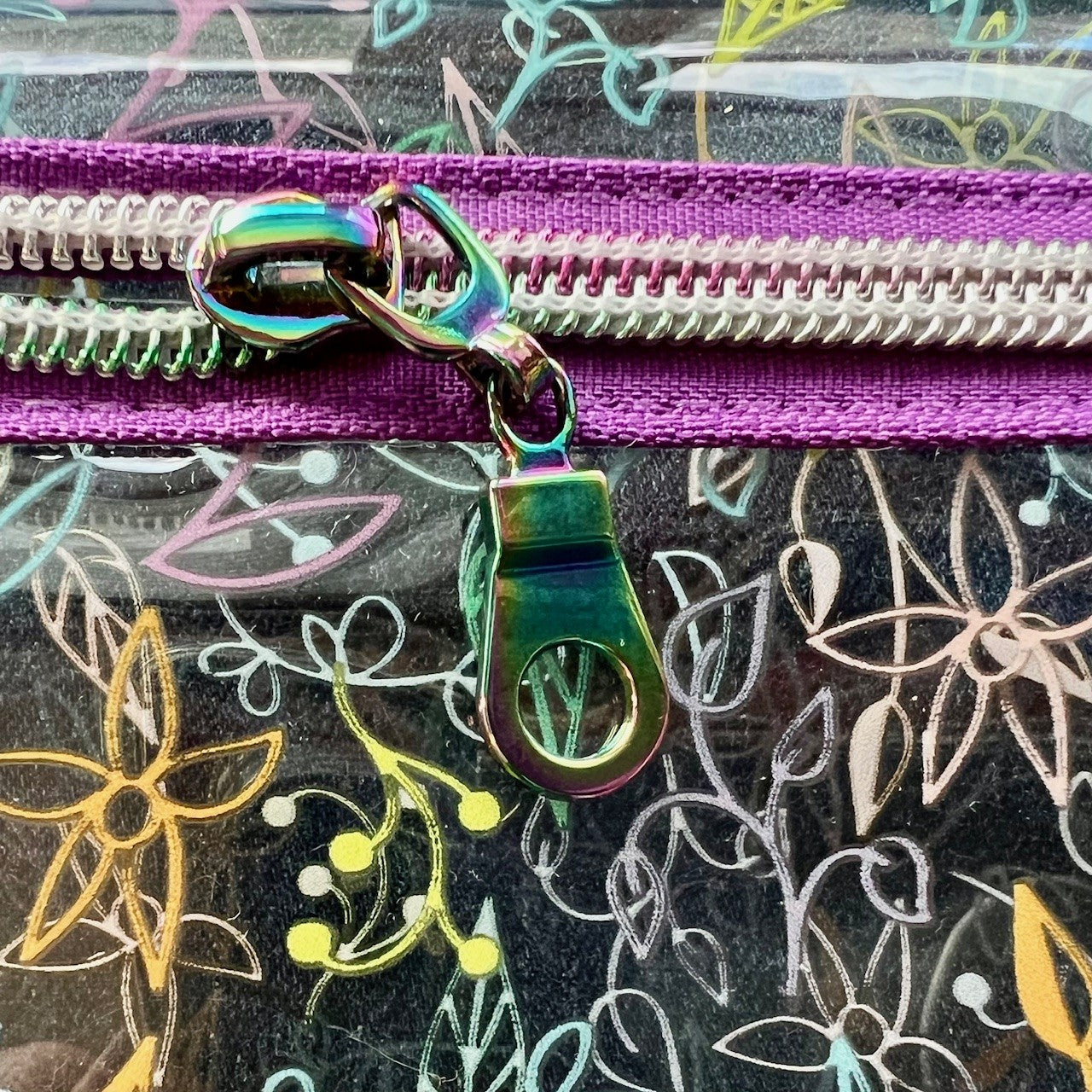 Clear see-through vinyl zipper pouch with floral pattern - showing a close-up view of the zipper pull.
