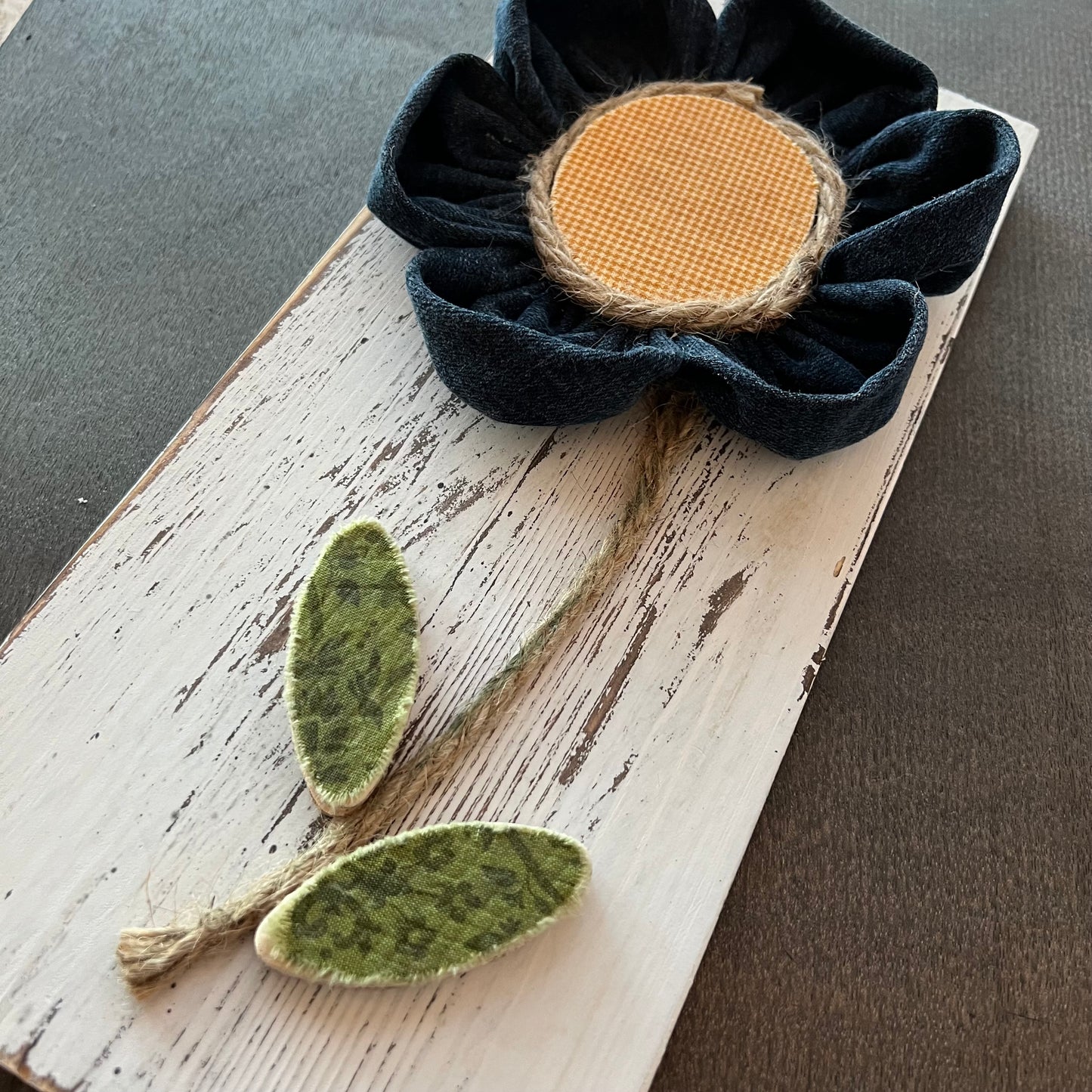 Close-up of the 3D botanical wall art featuring yellow gingham and reclaimed denim flowers on a white-washed wood plank.