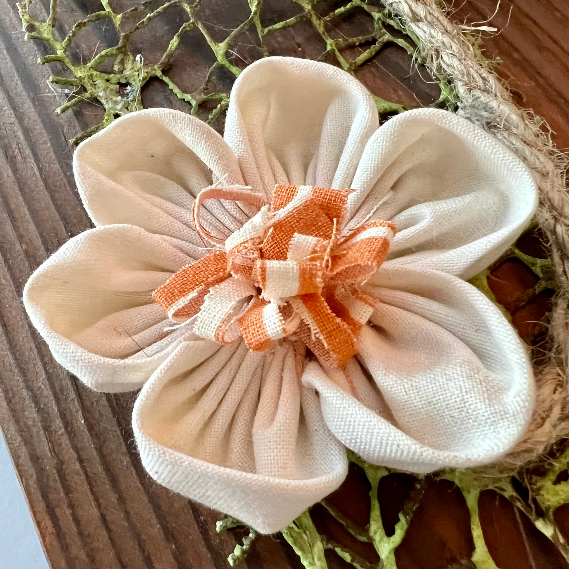 Close-up of the 3D botanical wall art featuring cream-colored flowers made from reclaimed fabric and mounted on a dark wood plank.