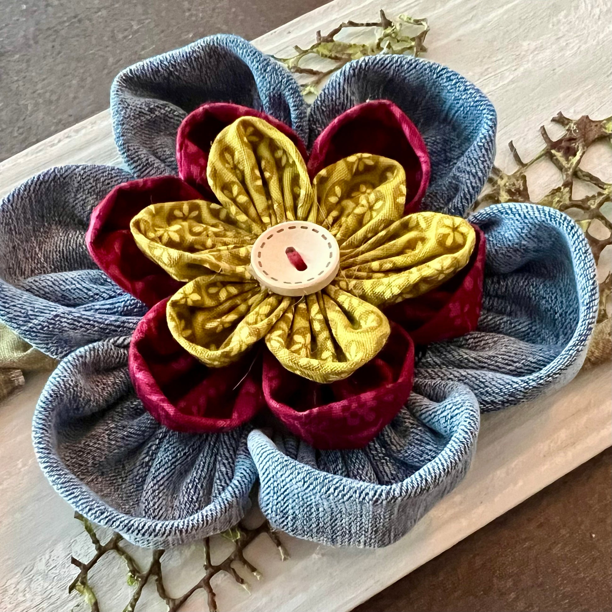 Close-up of the 3D botanical wall art featuring reclaimed denim and jewel-tone flowers on a distressed and painted wood plank. 