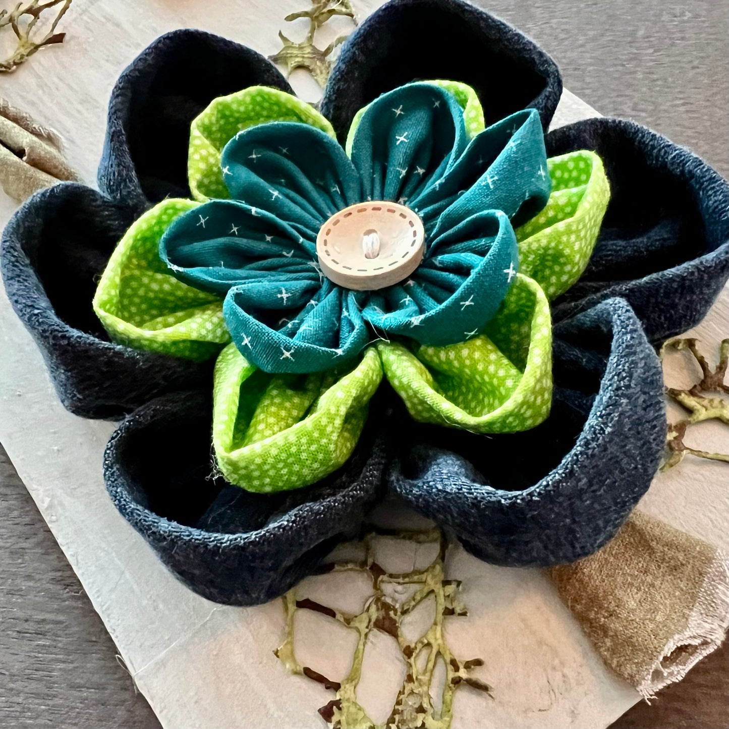 Close-up of the 3D botanical wall art featuring reclaimed denim and jewel-tone flowers on a distressed and painted wood plank. 