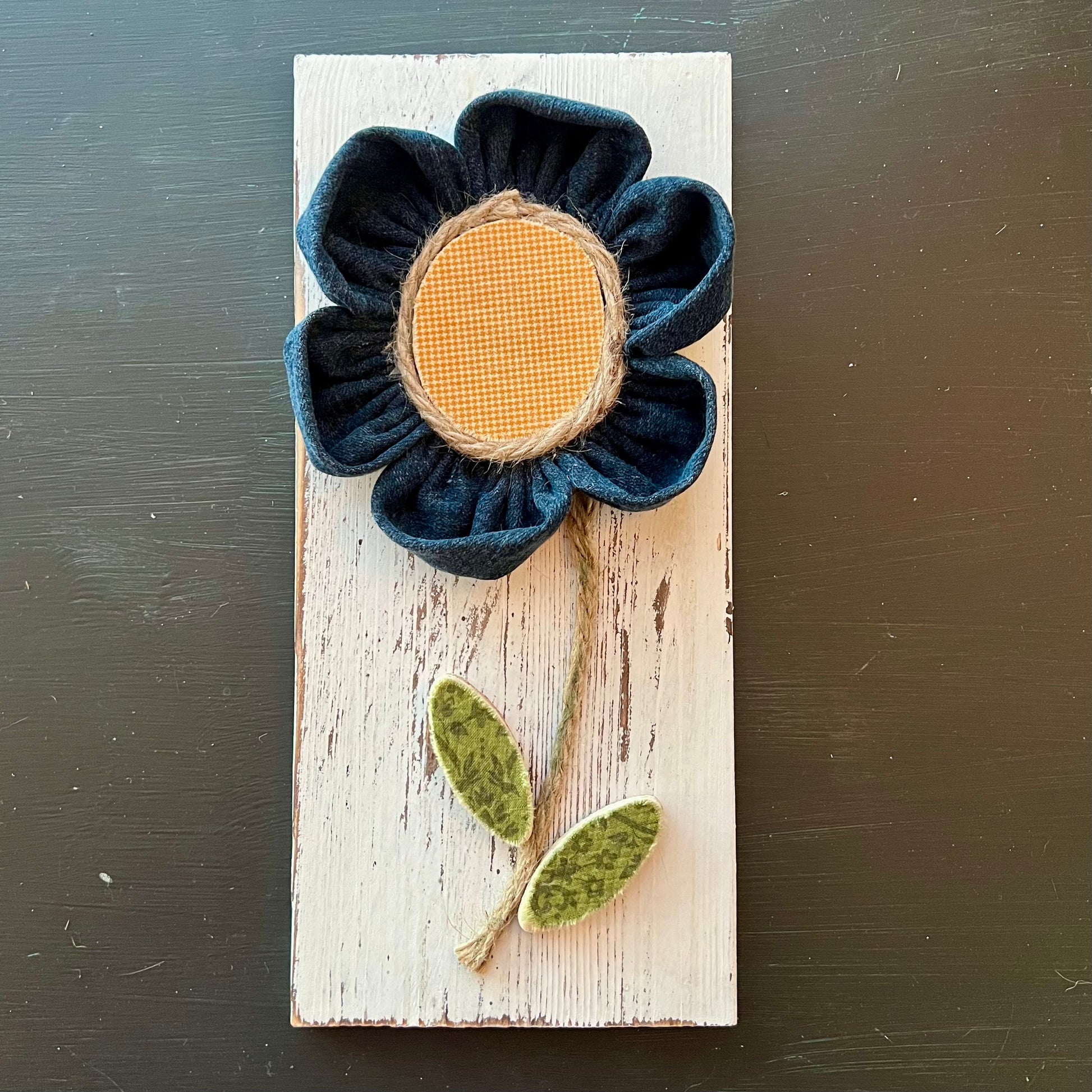 3D botanical wall art featuring yellow gingham and reclaimed denim flowers on a white-washed wood plank.