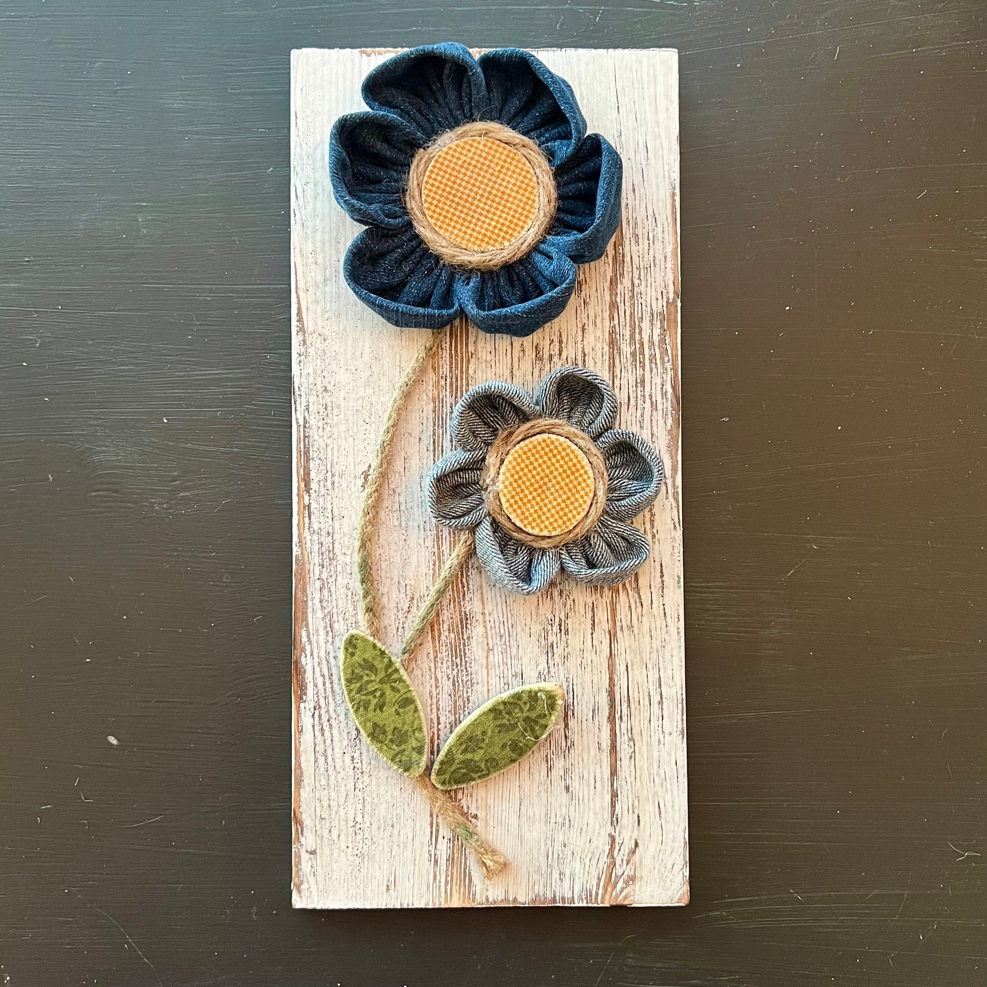 3D botanical wall art featuring yellow gingham and reclaimed denim flowers on a white-washed wood plank.