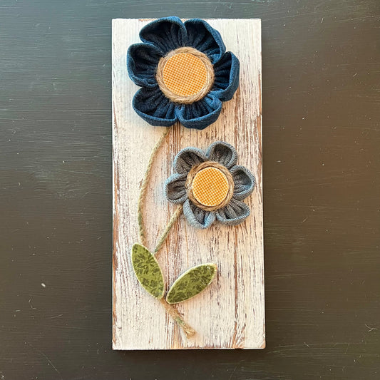3D botanical wall art featuring yellow gingham and reclaimed denim flowers on a white-washed wood plank.