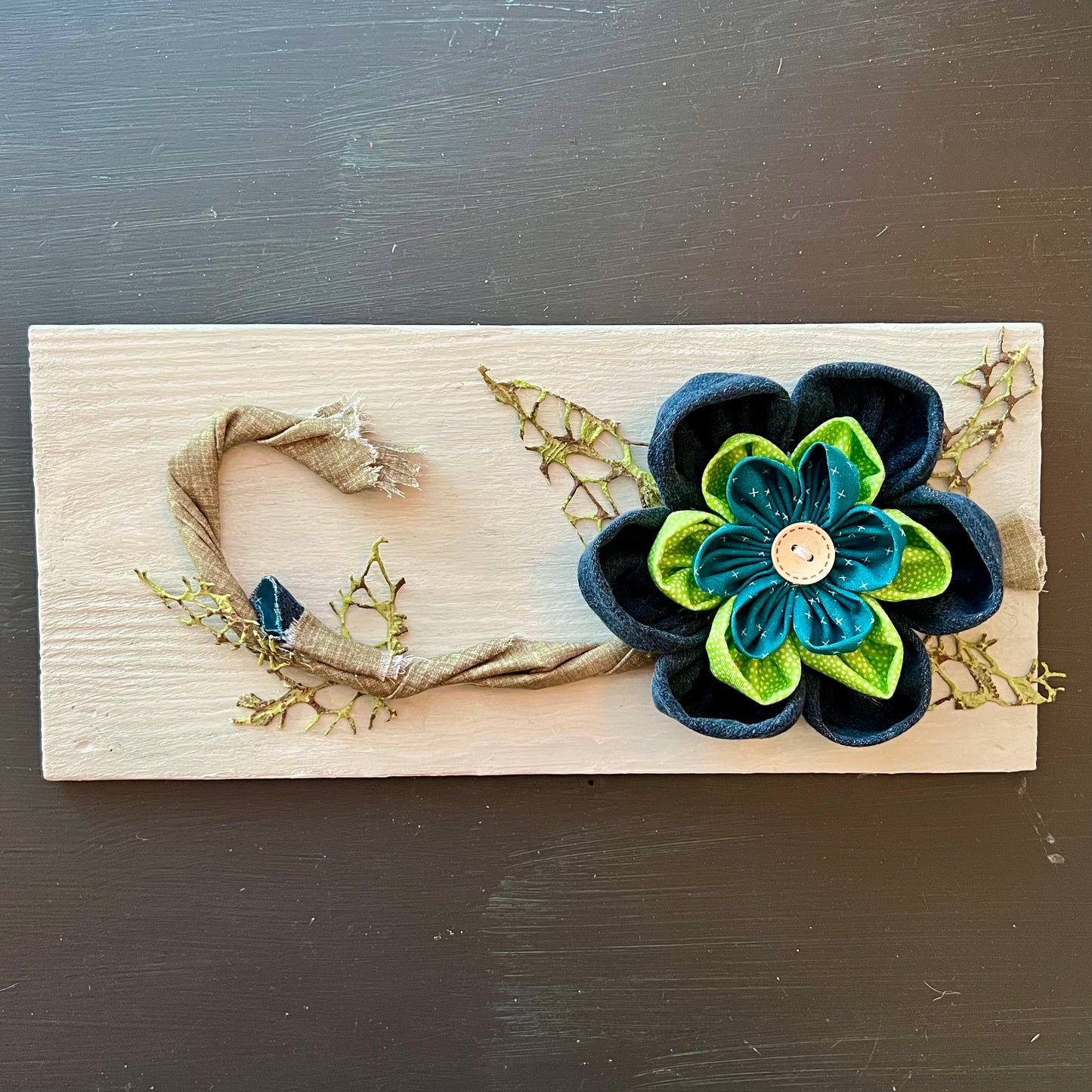 3D botanical wall art featuring reclaimed denim and jewel-tone flowers on a distressed and painted wood plank. 