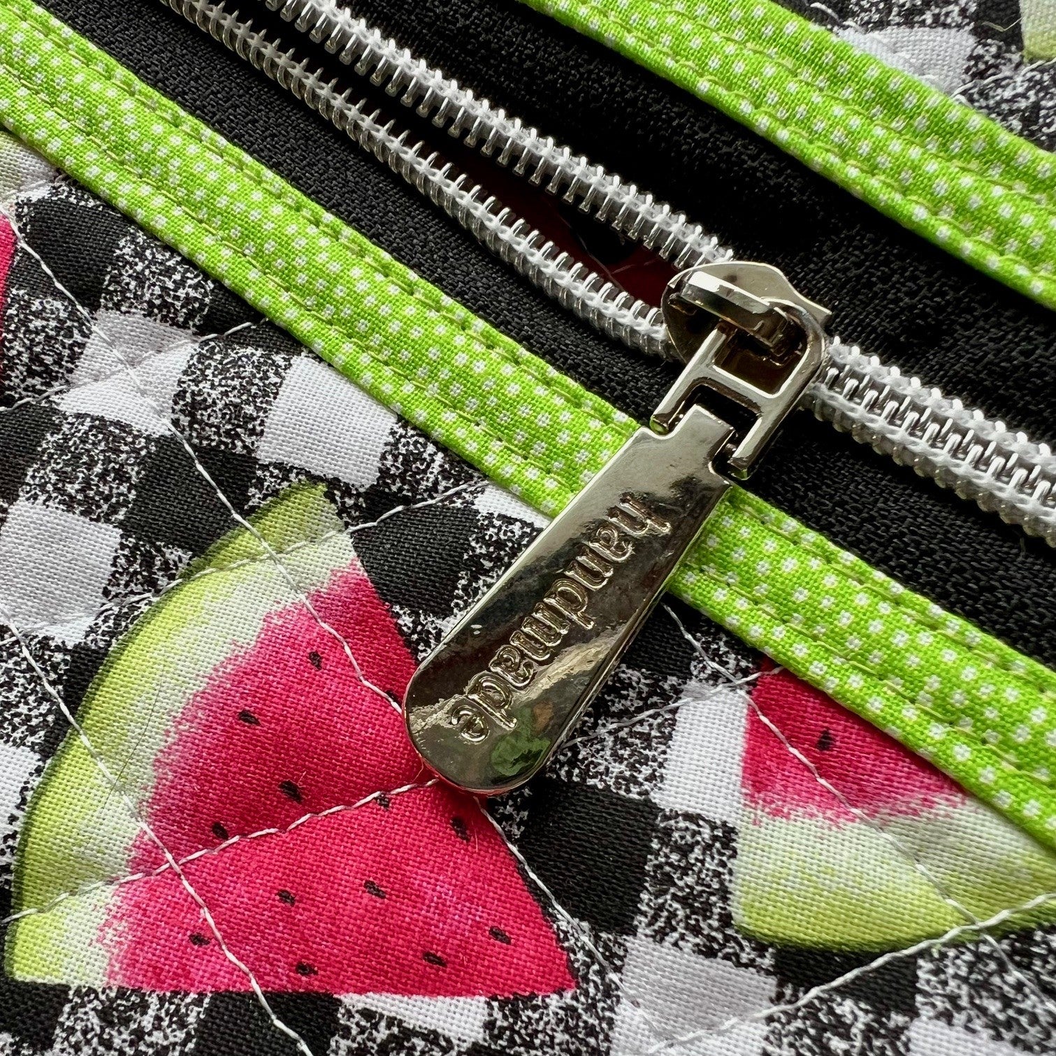 Close up of the quilted zipper pouch, showing a silver zipper pull that says "handmade."