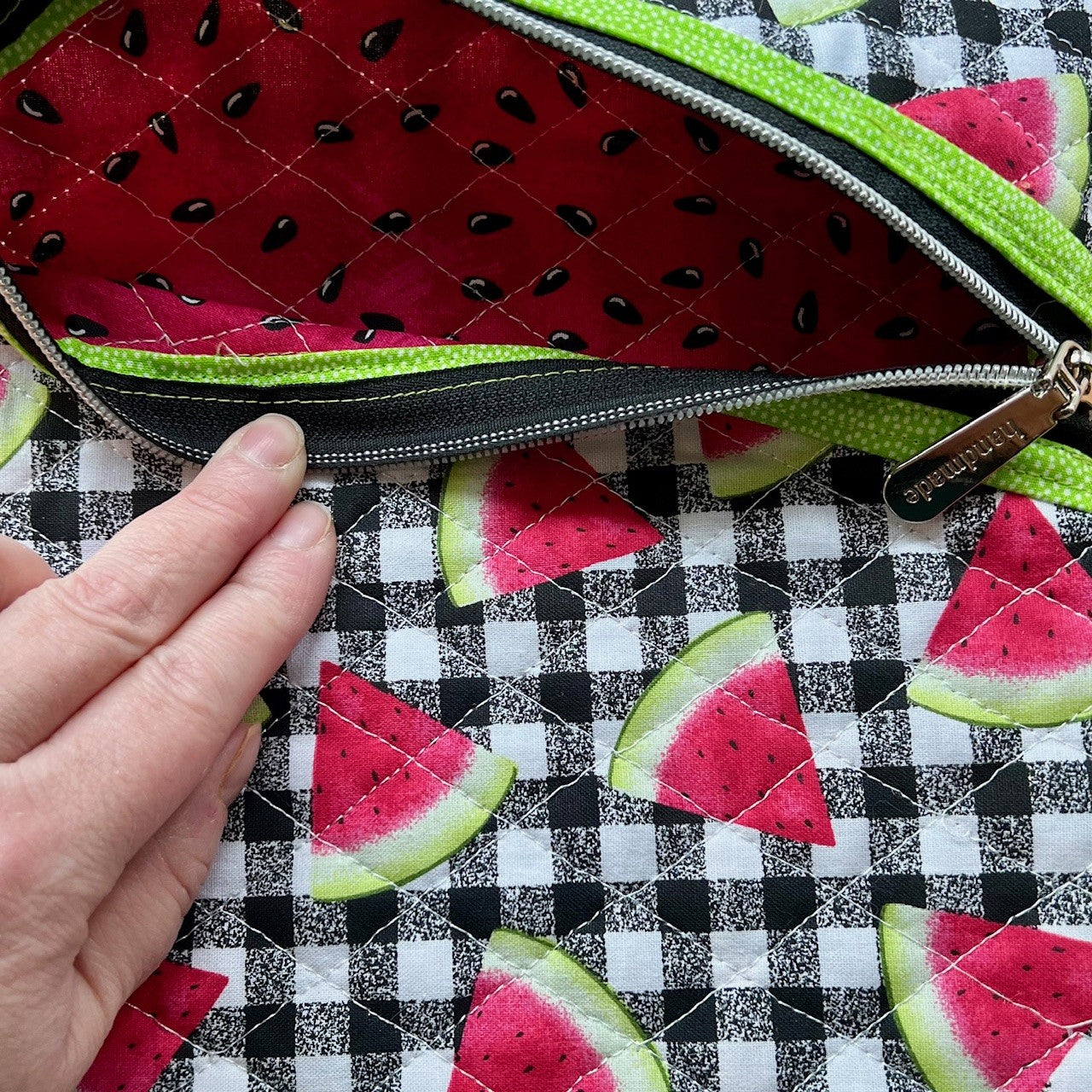 Inside the quilted zipper pouch is a pink fabric with seeds, like the inside of a watermelon.